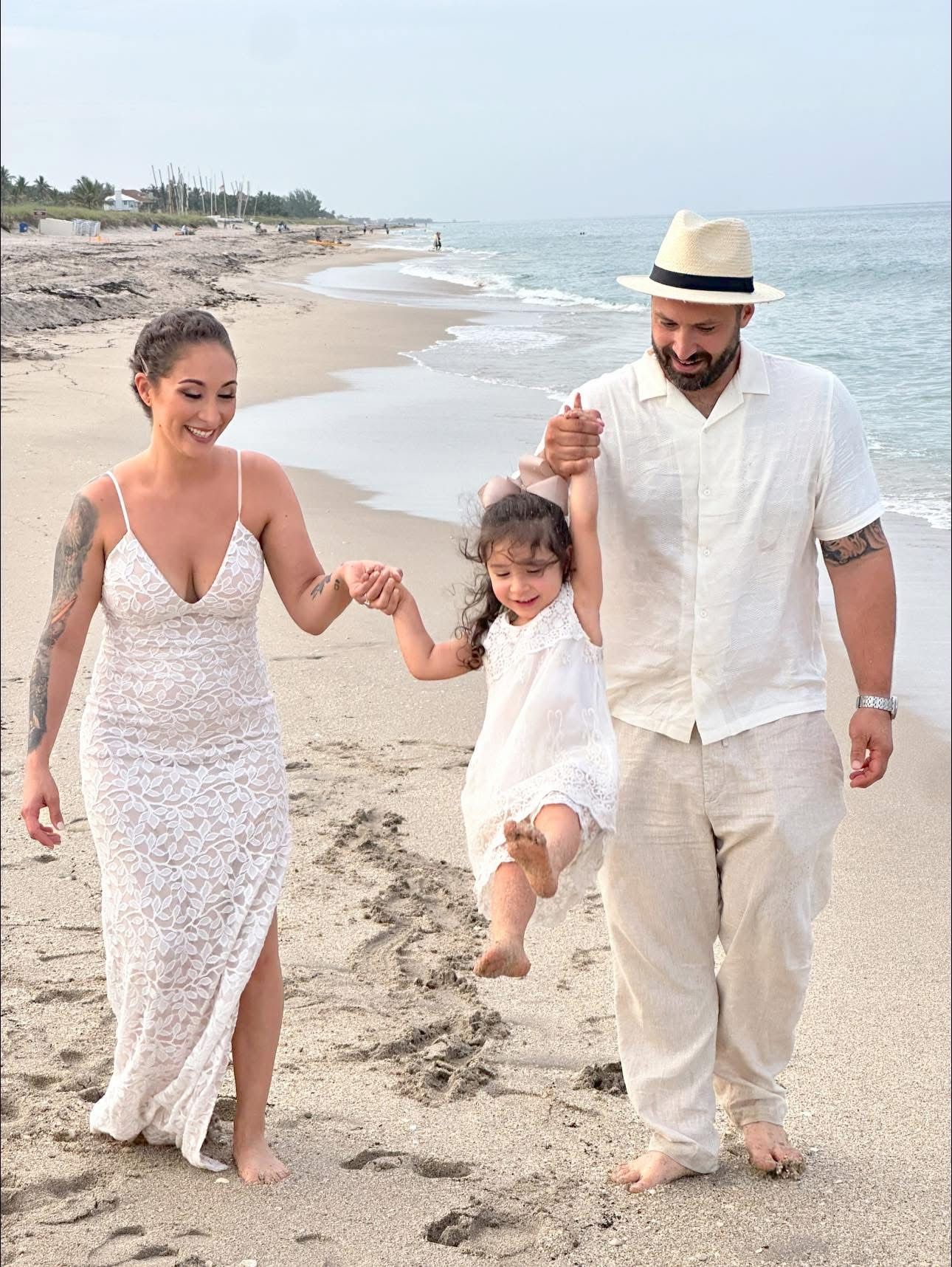 Family taking a stroll along a sunny beach with a young child wearing white clothes.