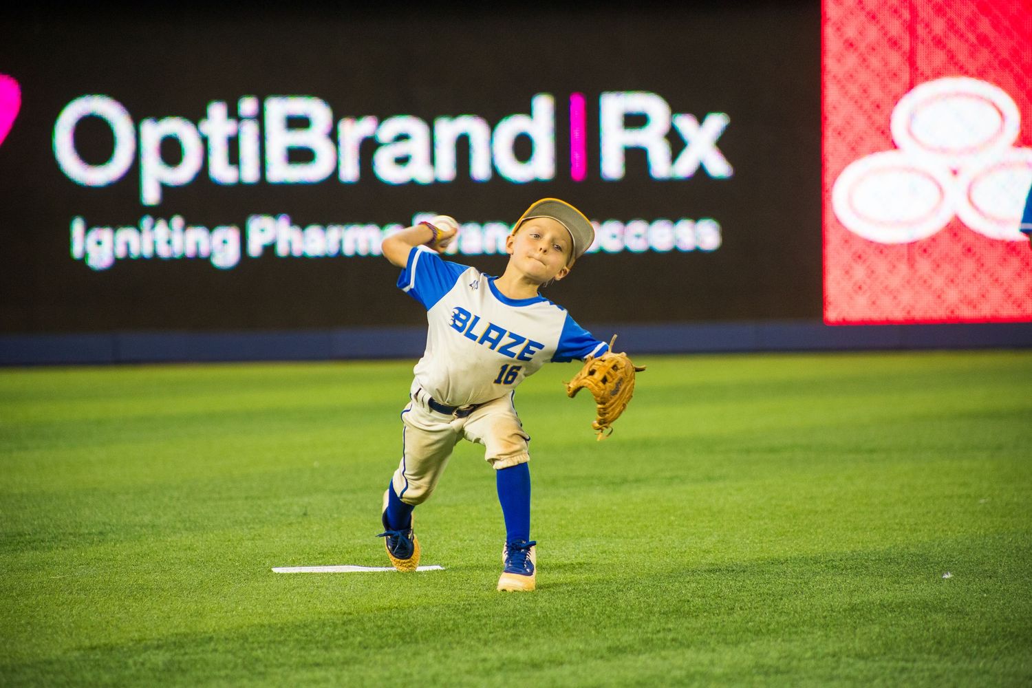 Young baseball player in blue uniform practicing fielding stance on green turf.