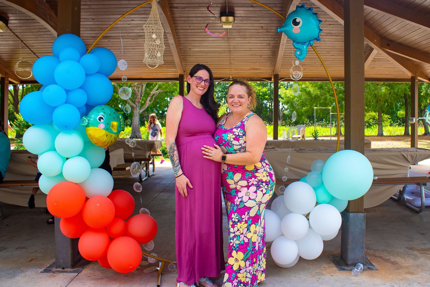 Festive baby shower gathering with colorful balloon arch and decorations in an outdoor pavilion.