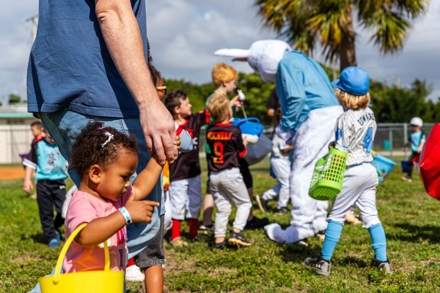 A young girl holds a yellow Easter basket while participating in a festive outdoor Easter egg hunt event.