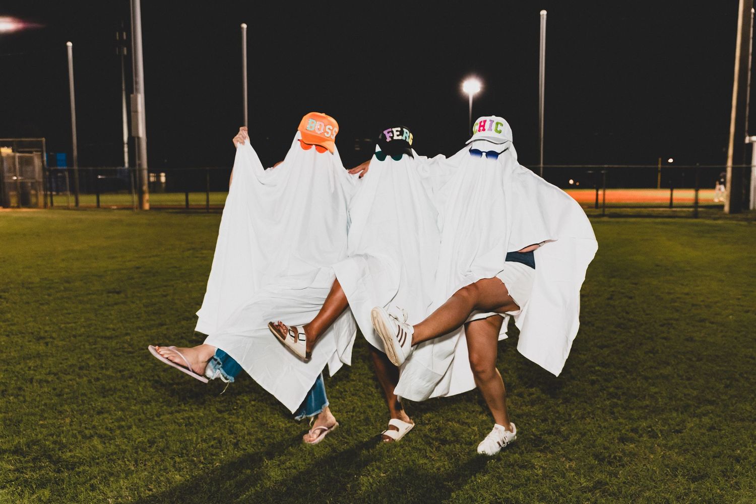 People wearing ghost costumes made from white sheets sit together on grass at night.