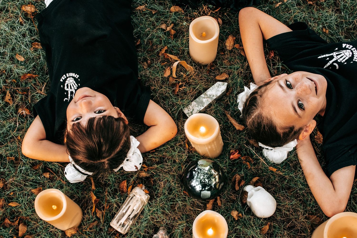Two women lying on grass surrounded by candles and bottles in an intimate outdoor setting.