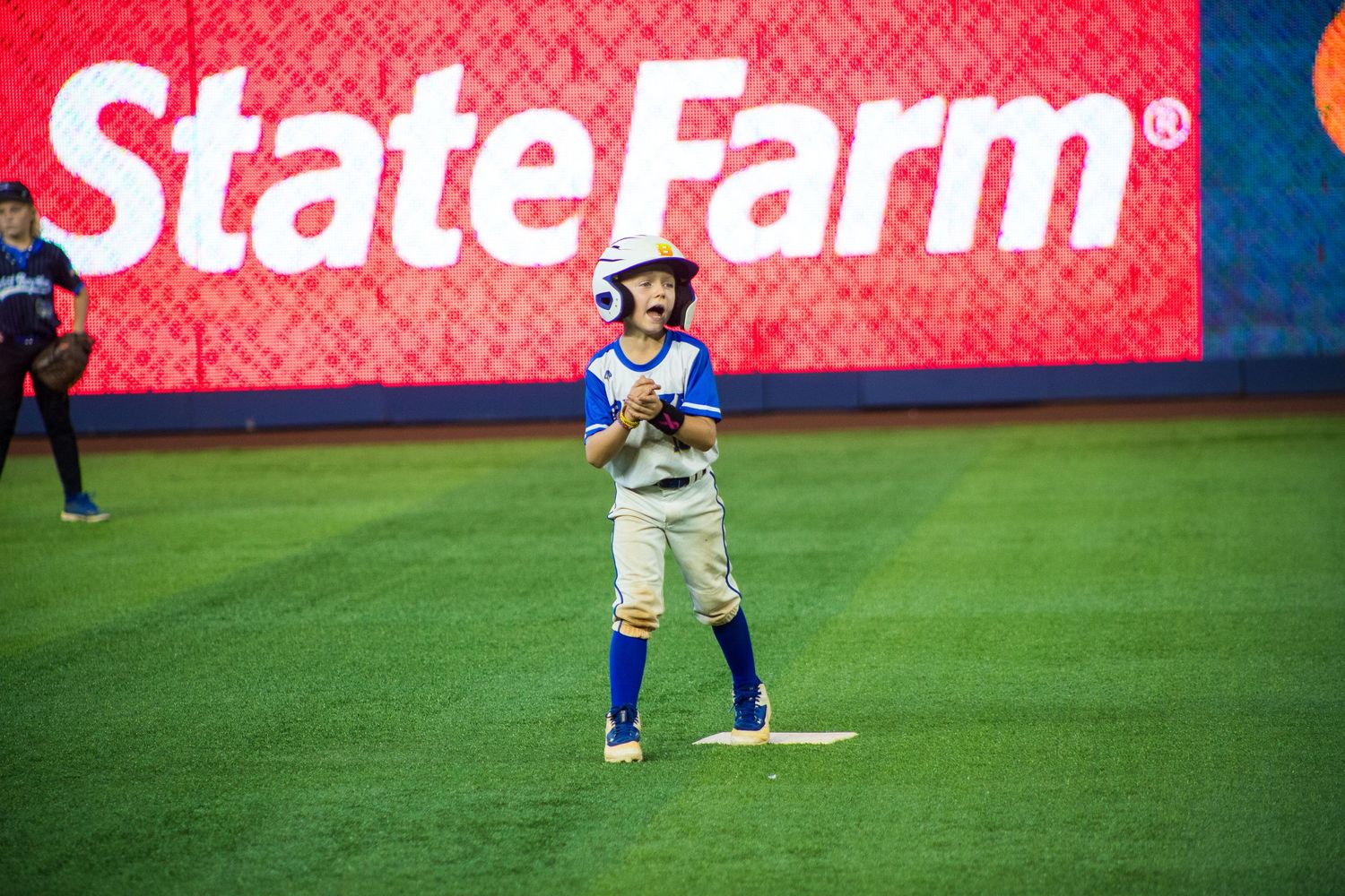Baseball player stands ready at bat in front of red State Farm advertisement sign.