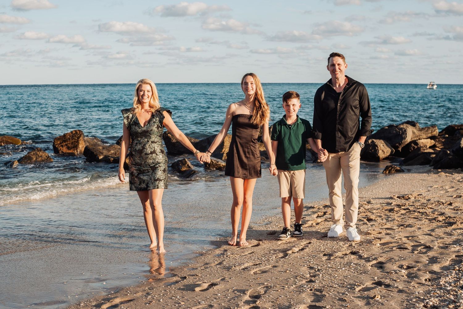 Family of four taking a beach walk together near rocky coastline during golden hour.