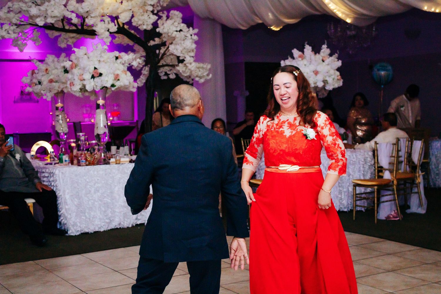 Wedding reception hall decorated with pink lighting, floral arrangements and elegant white draping.