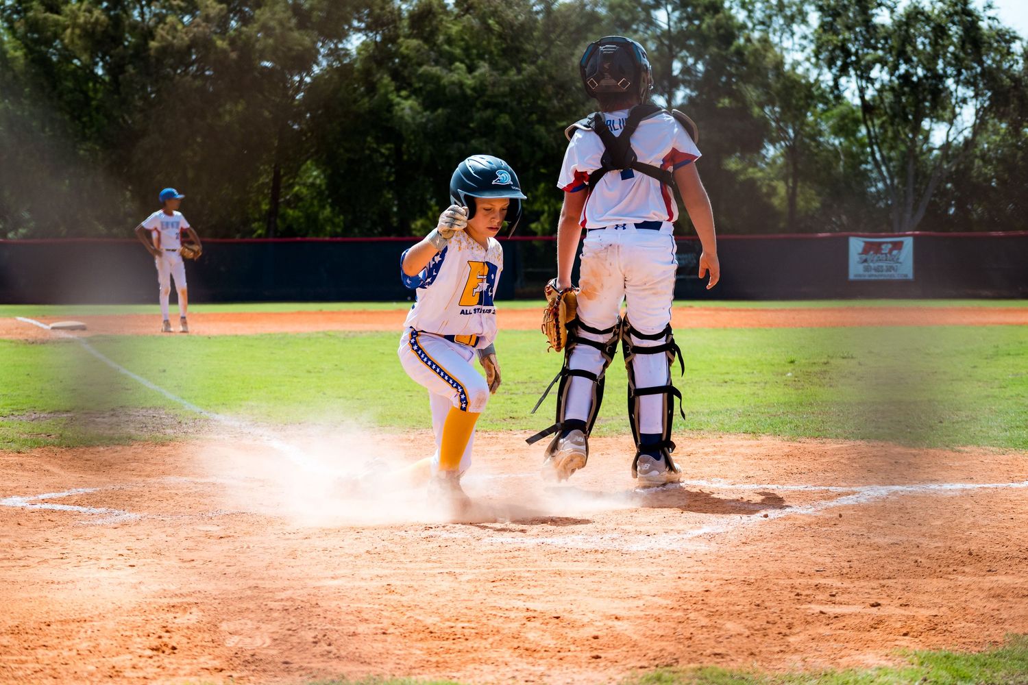 Baseball player slides into home plate while catcher attempts to make the tag during an intense game play.