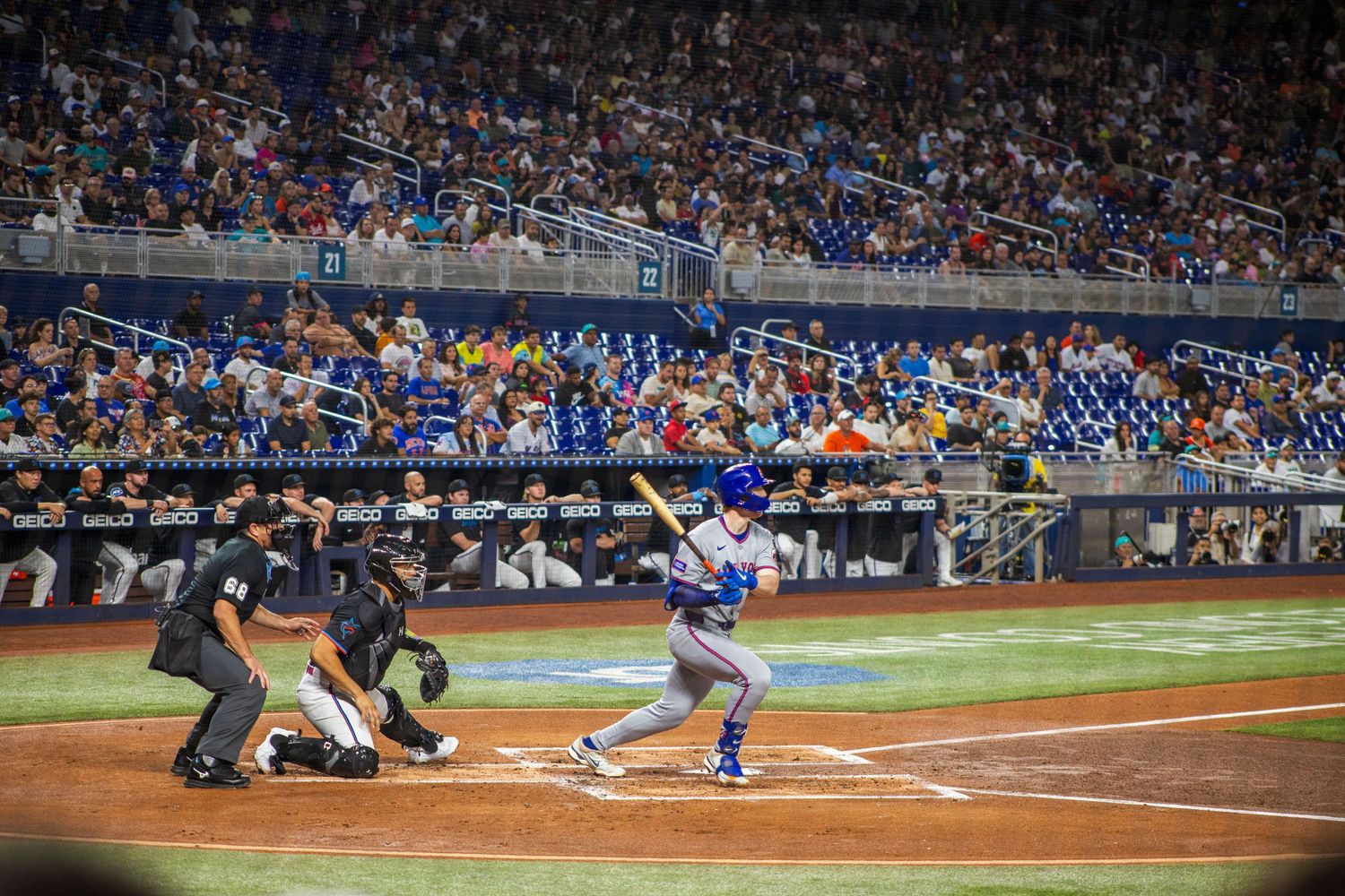 Baseball players in action at home plate during a professional night game with stadium lights illuminating the field.