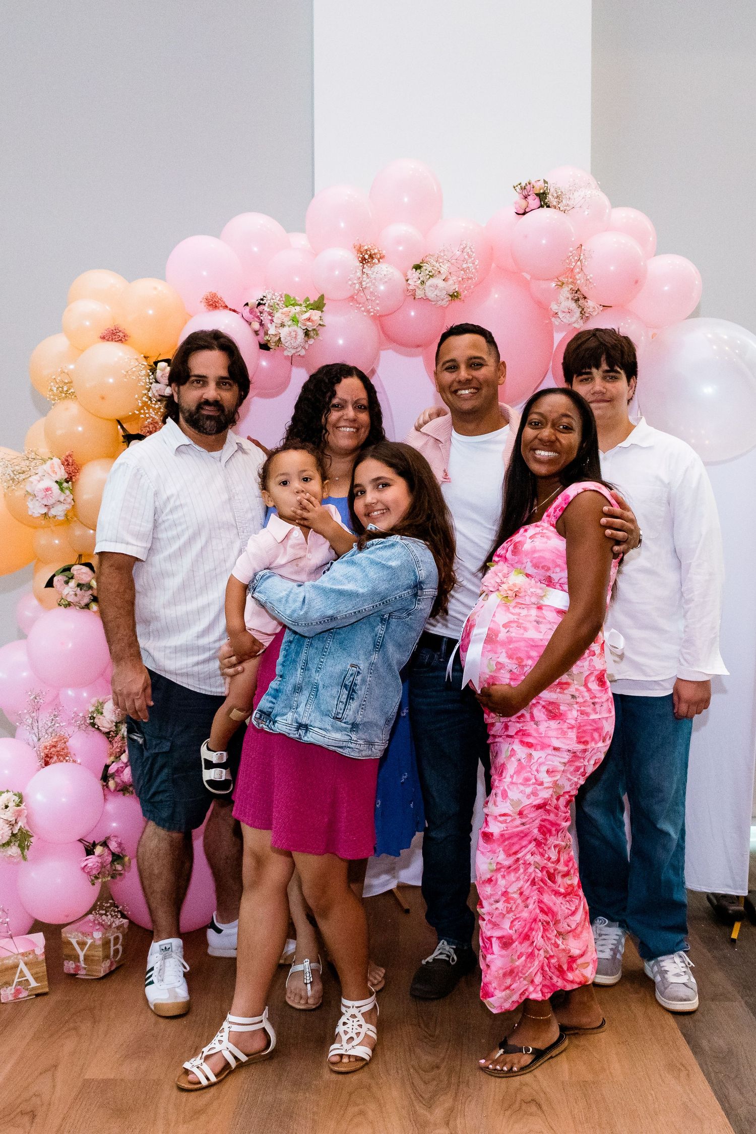 Family group photo in front of pink balloon arch at celebration event.