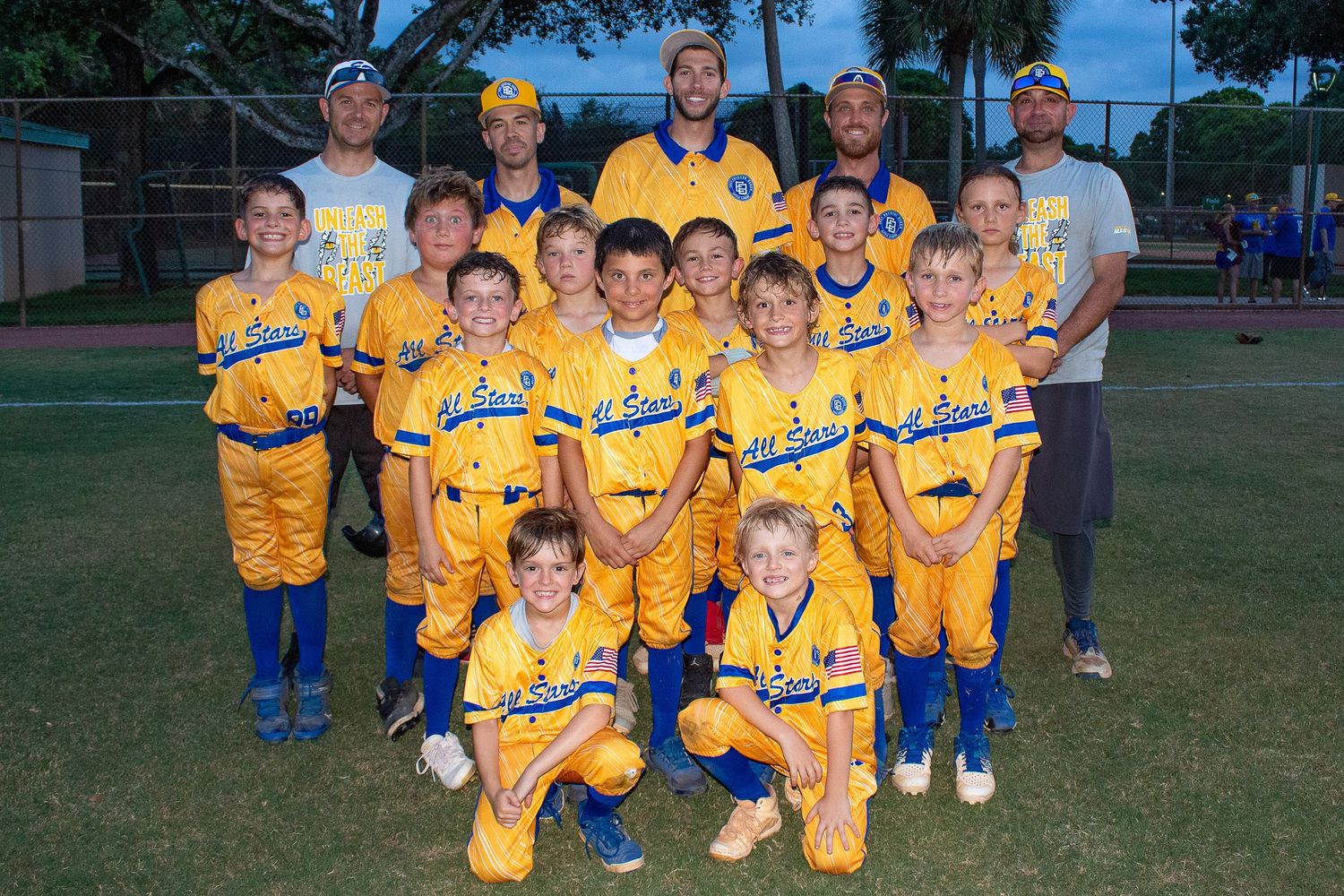 Youth baseball team poses for formal group photo wearing matching yellow and blue uniforms.