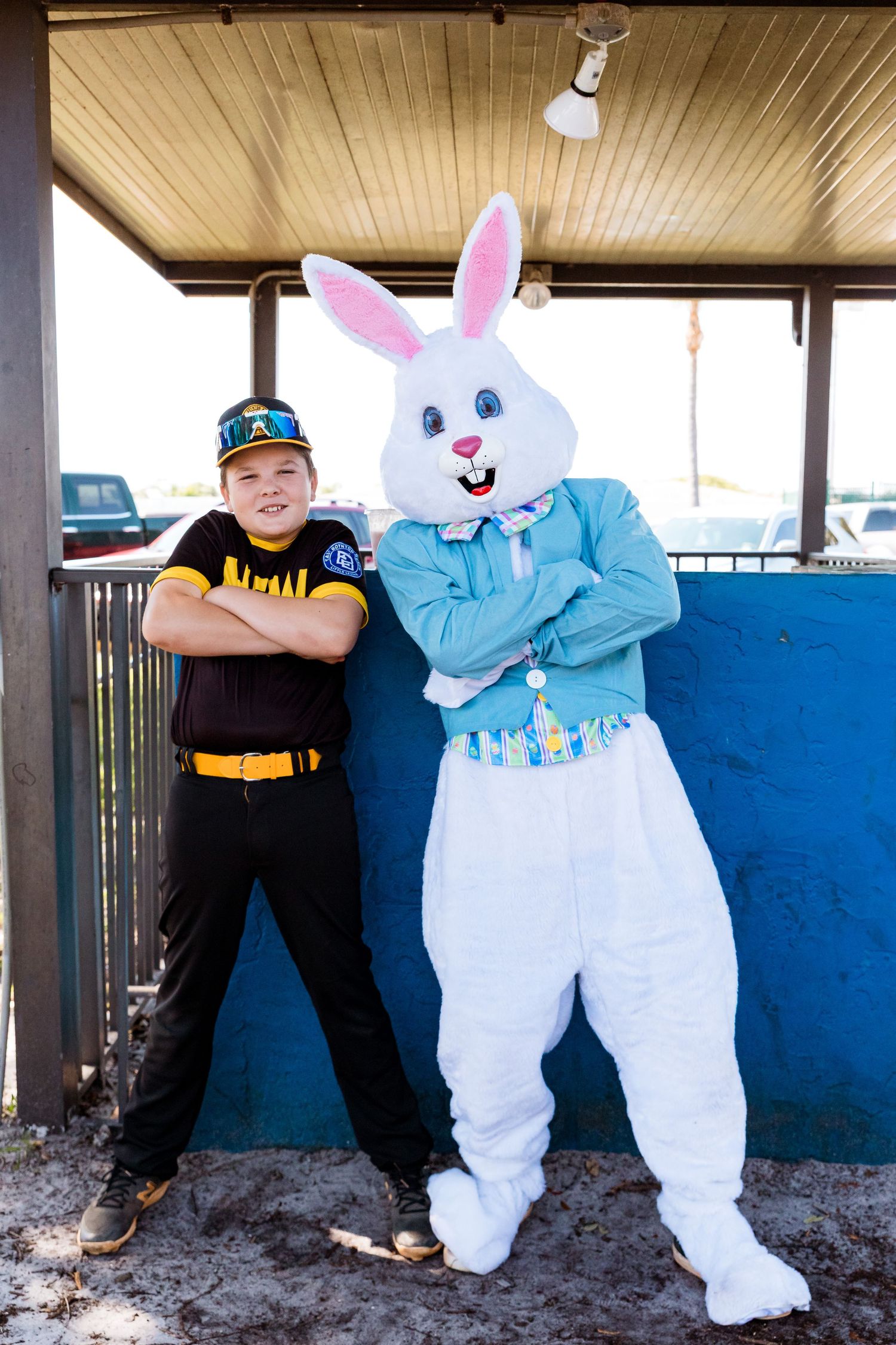 The Easter Bunny in a blue jacket poses with a young athlete wearing a baseball uniform.