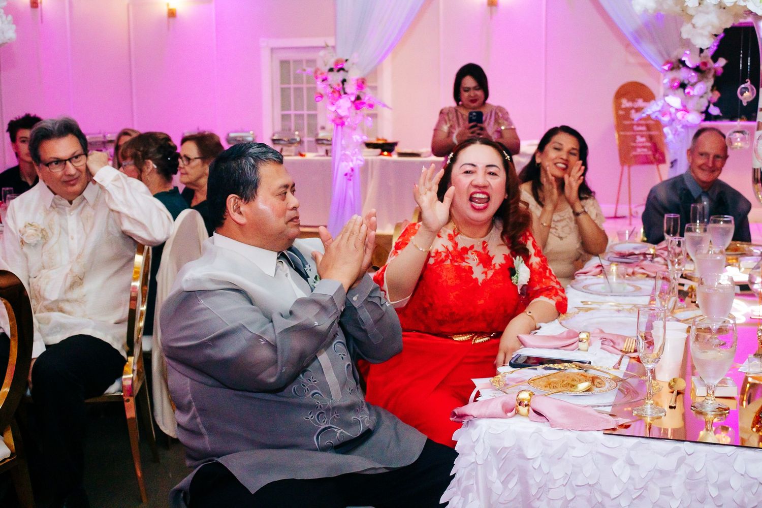 Wedding reception celebration showing dining tables with pink ambient lighting and guests enjoying the festivities.