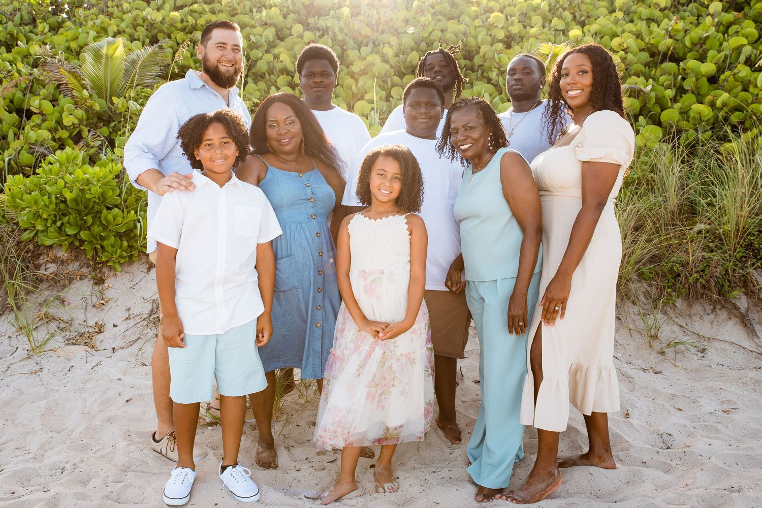 A group in coordinated white and blue outfits poses together on a sandy beach at sunset.