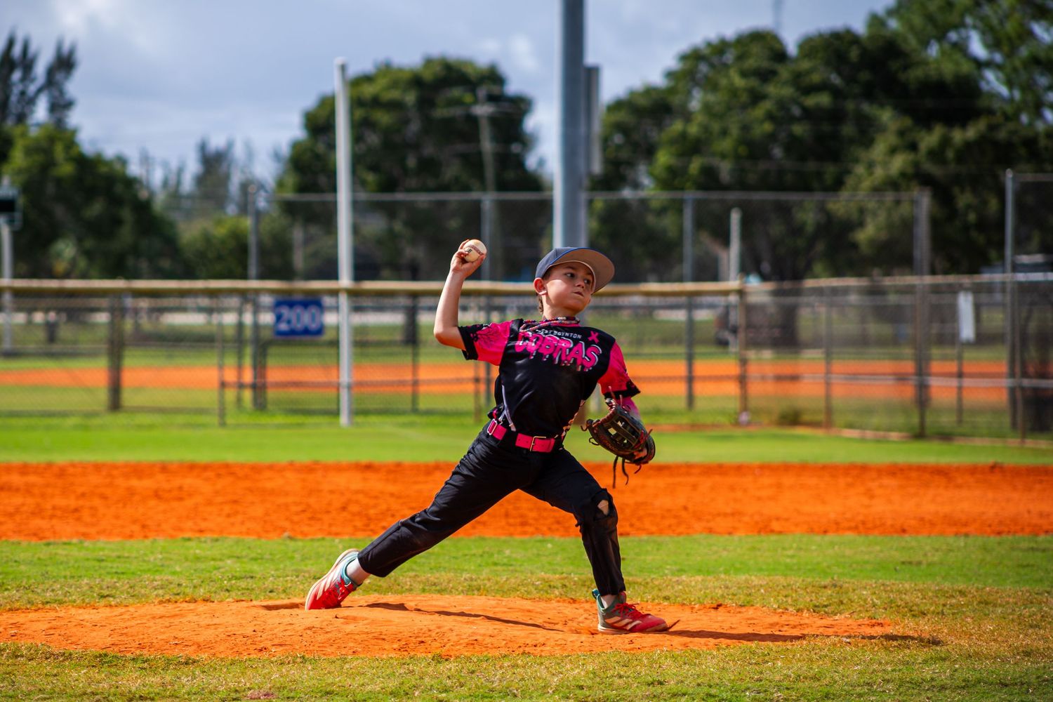 Baseball player in black uniform stretches to make a diving catch on the infield dirt during a game.