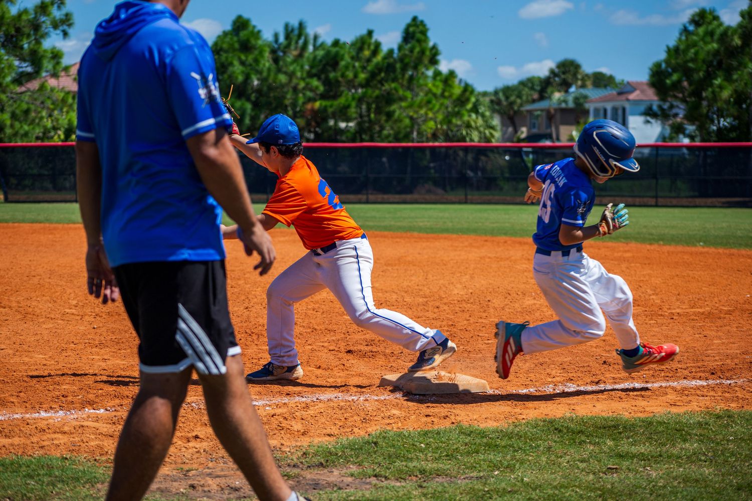 Baseball player sliding into home plate during a youth baseball game on a dirt field surrounded by grass.