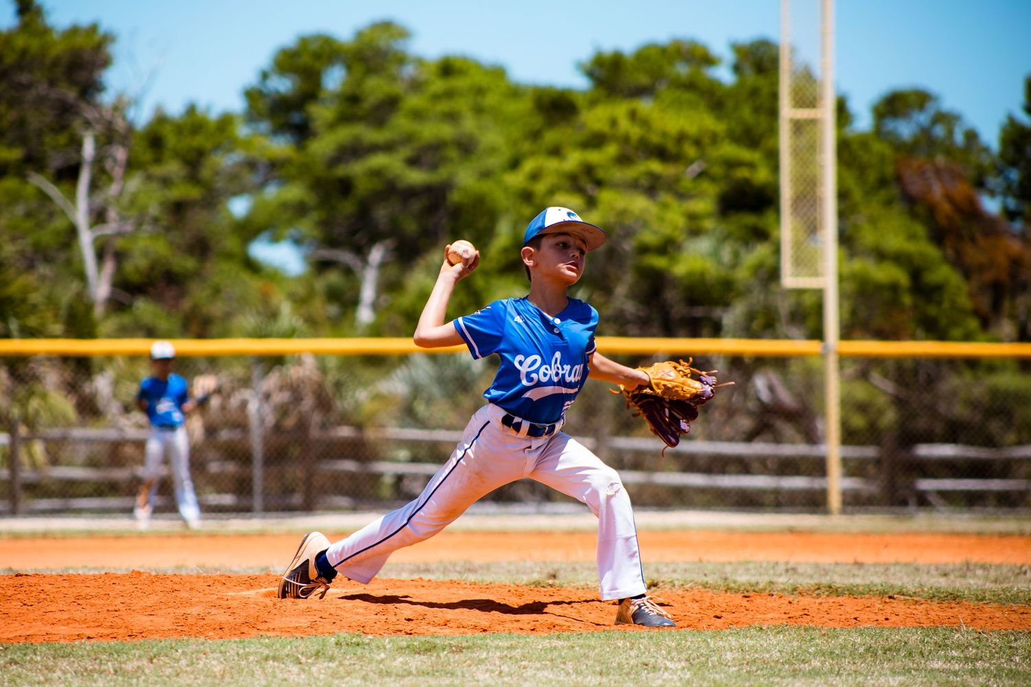 Baseball player in blue jersey throwing a pitch on dirt mound during game.