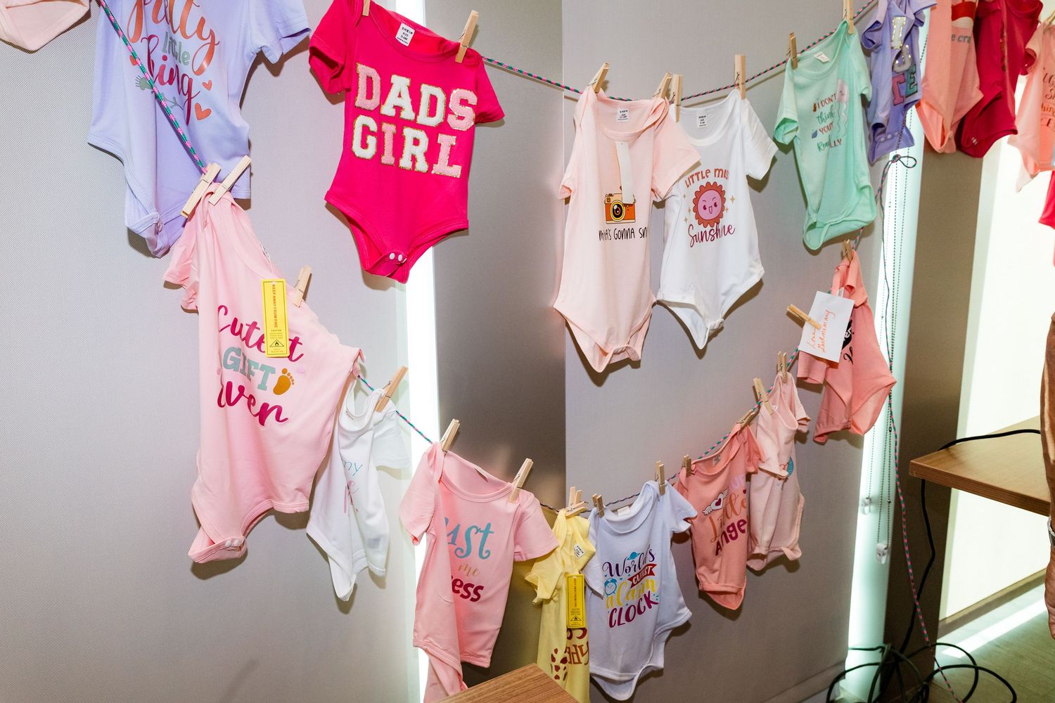 Baby onesies in pink and pastel colors displayed on a clothesline at a baby shower.