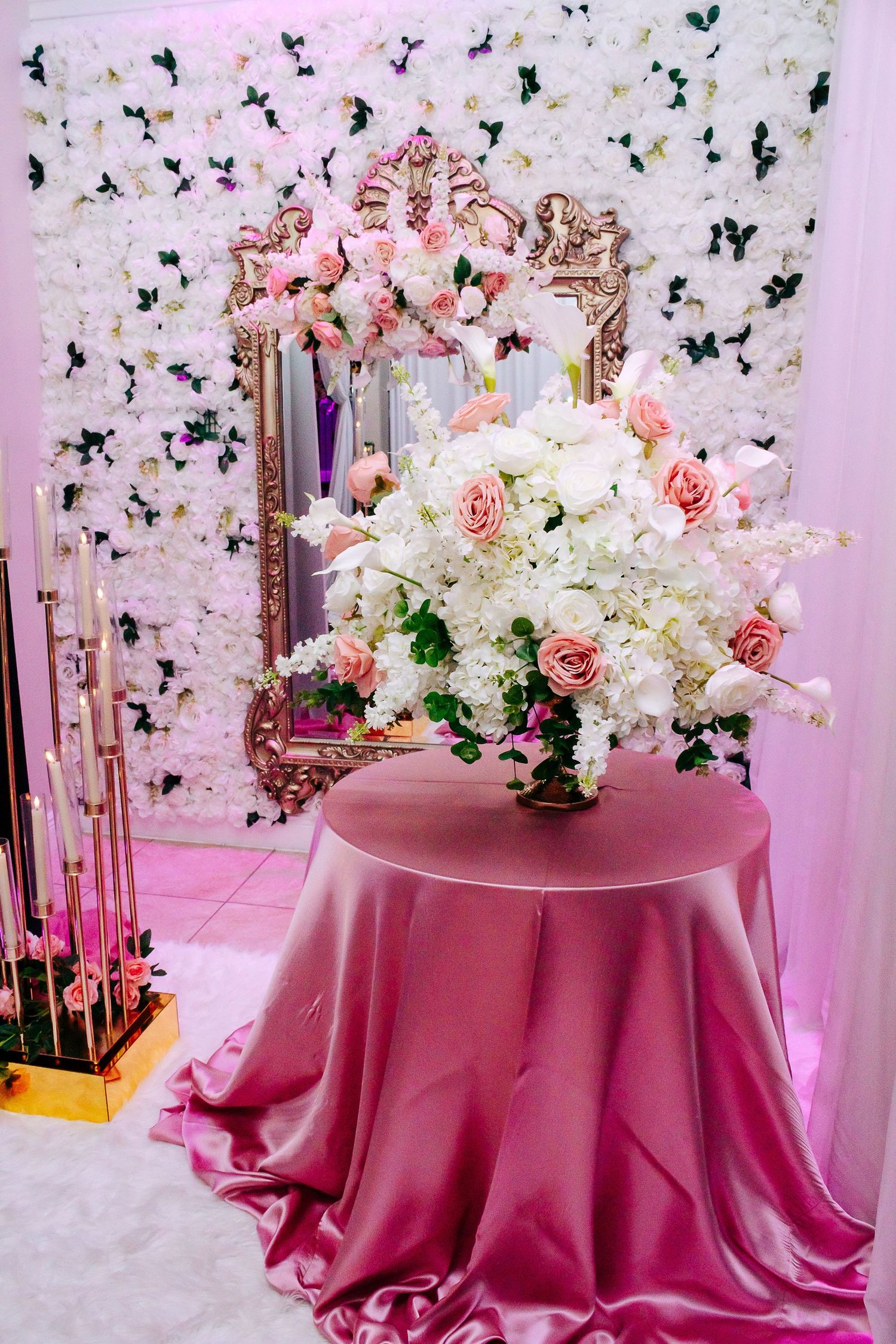 Elegant pink round tables with tall floral centerpieces against a butterfly-decorated wall backdrop.