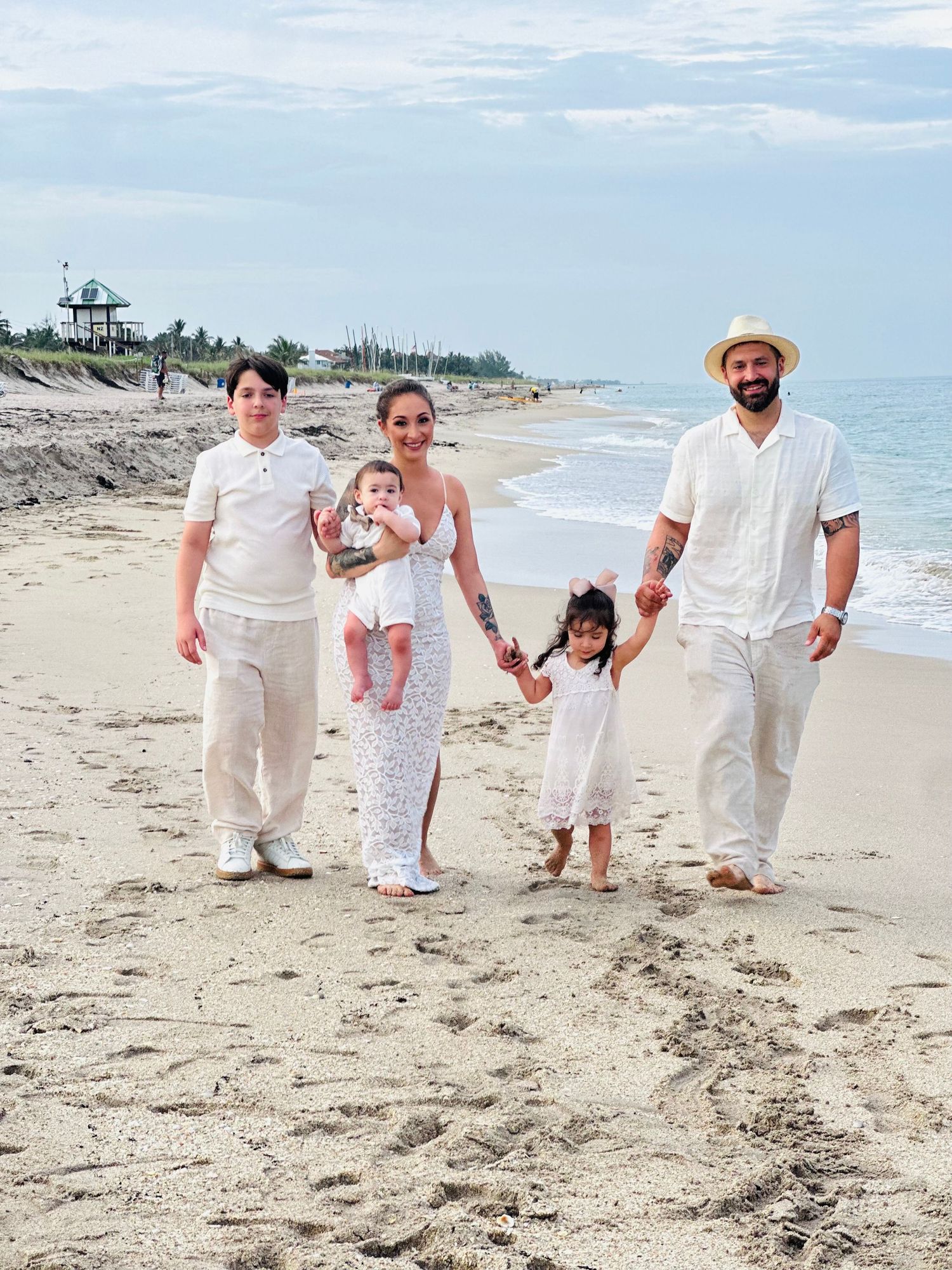 Family of four walking on beach wearing coordinated white outfits.