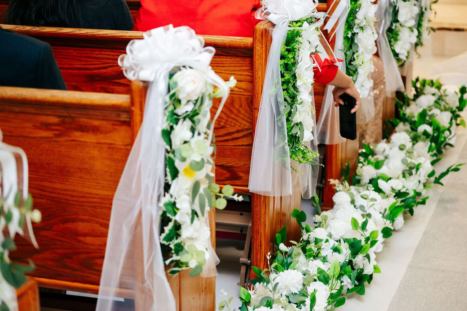 Church pews decorated with white tulle and greenery for wedding ceremony.