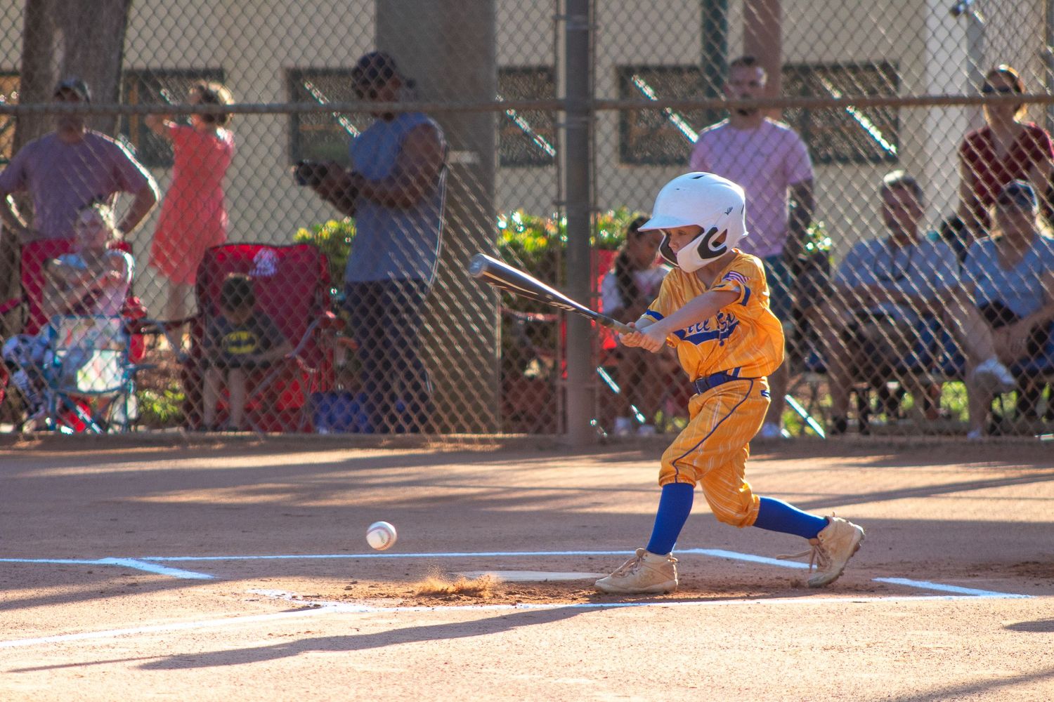 Baseball player in orange uniform swings bat during youth league game.