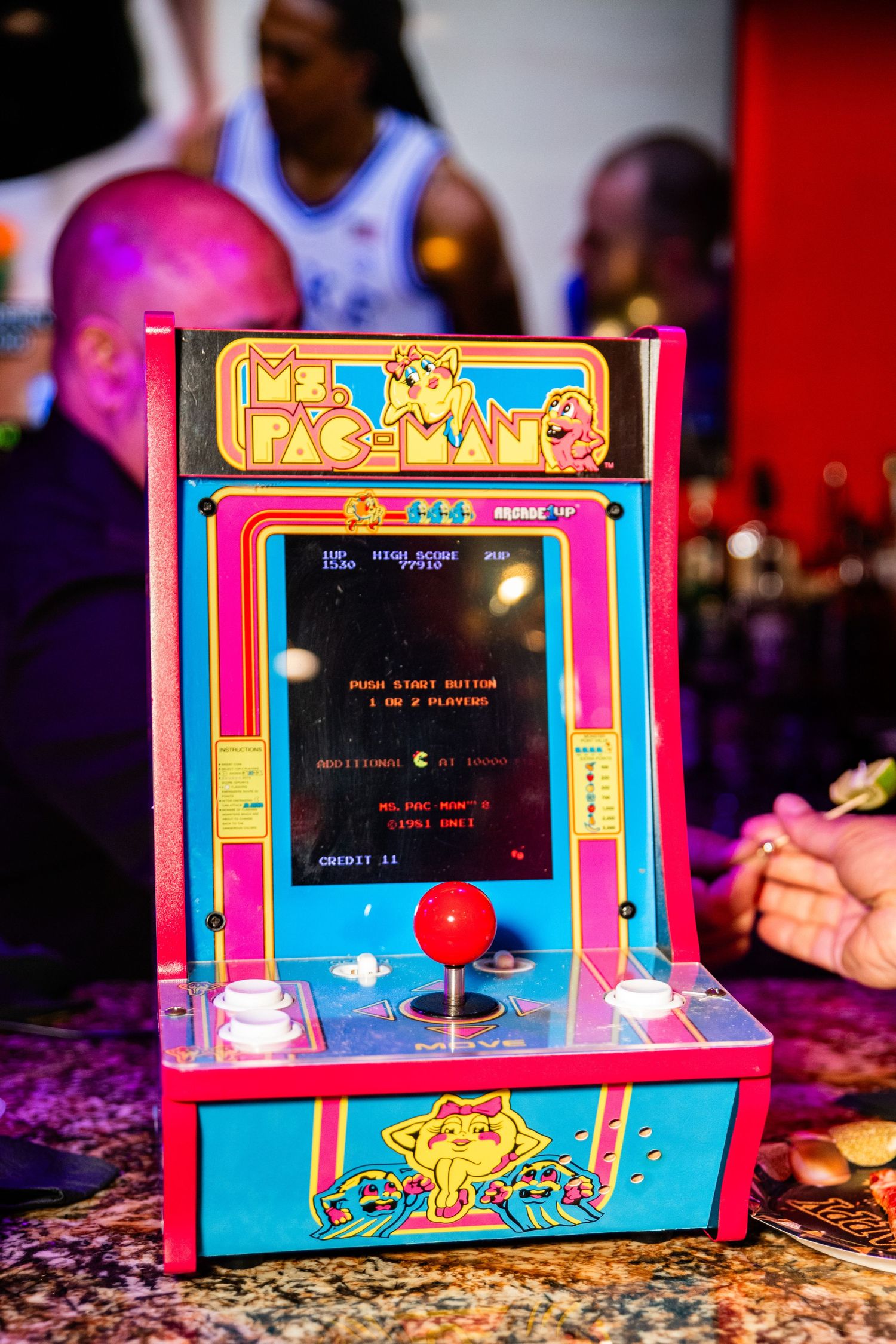 A colorful and retro-styled arcade game machine with a joystick and buttons, displaying a classic video game on the screen.