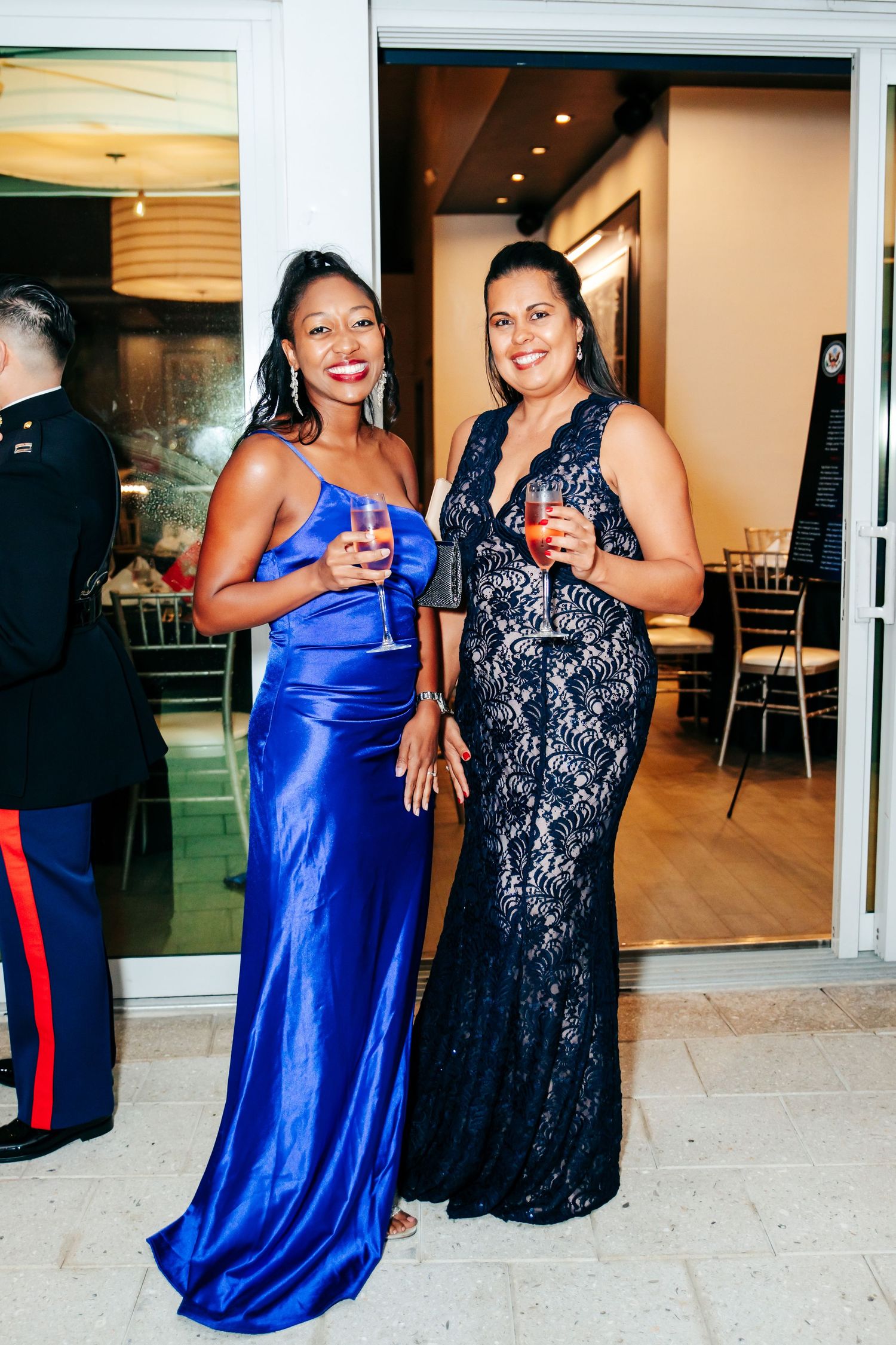 Two guests in formal attire, one in royal blue dress and one in black lace, celebrate at an event.