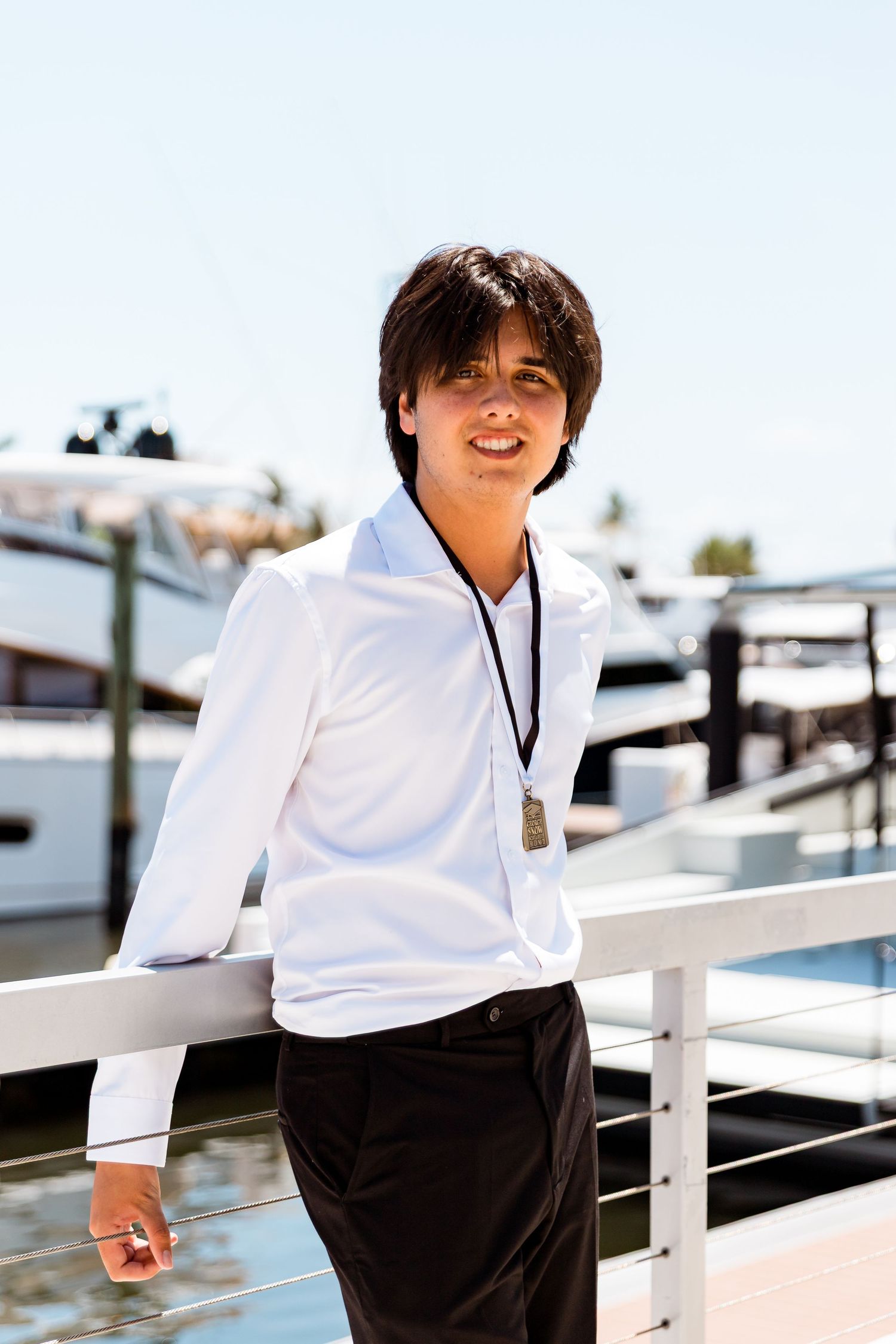 Person in a white long-sleeved top and black pants stands casually by a boat dock railing on a sunny day.