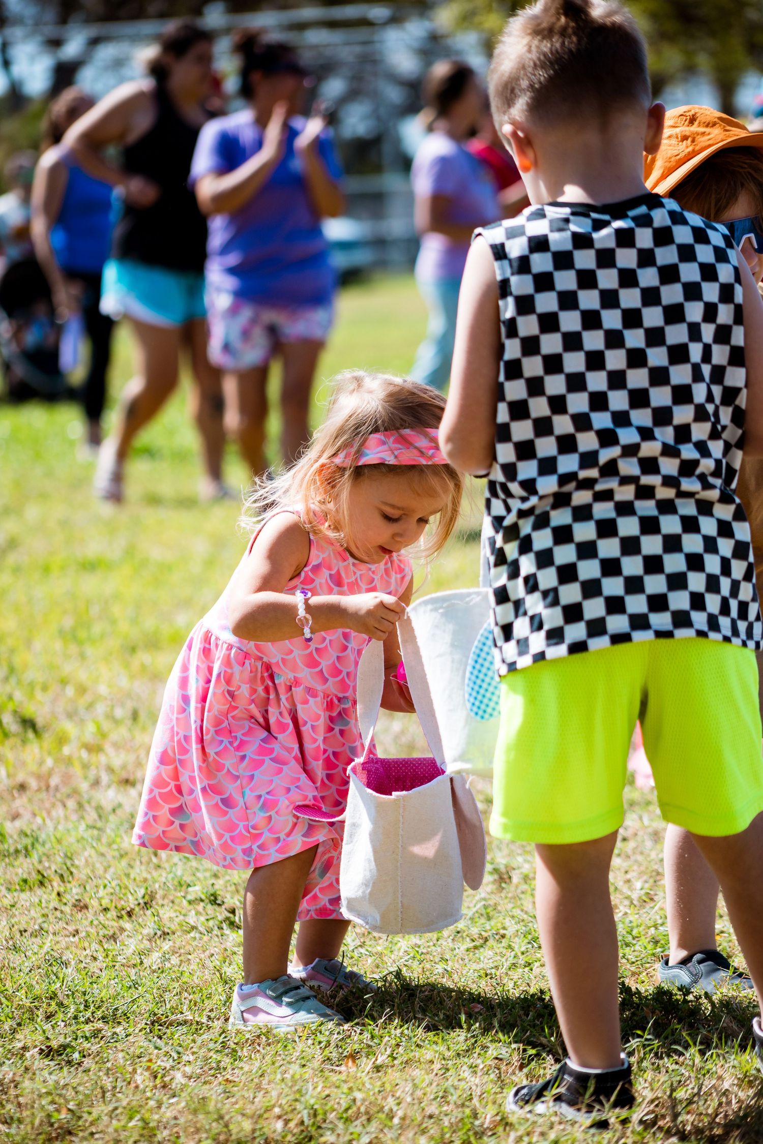 Children participate in an outdoor Easter egg hunt activity with baskets on a sunny day.