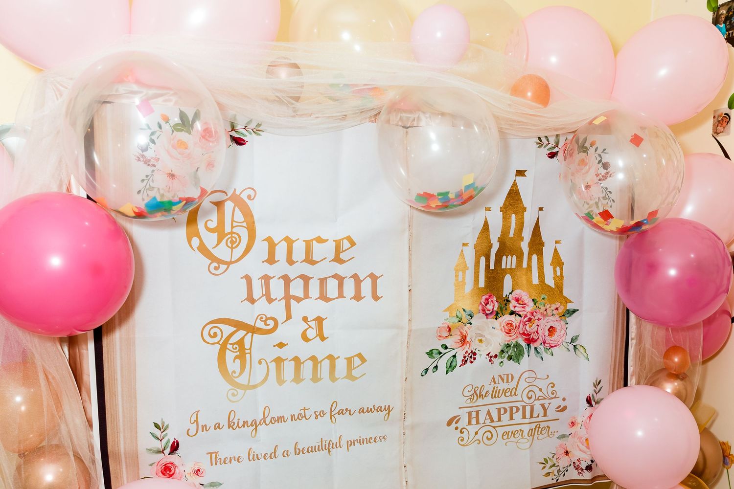 Princess party banner with pink and gold balloons and castle motif on wall.