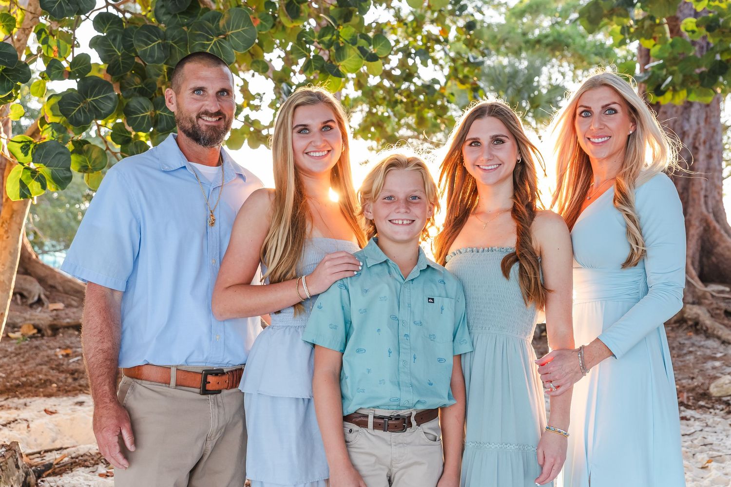 Extended family group dressed in matching blue and mint colored clothing smiles for outdoor portrait session.