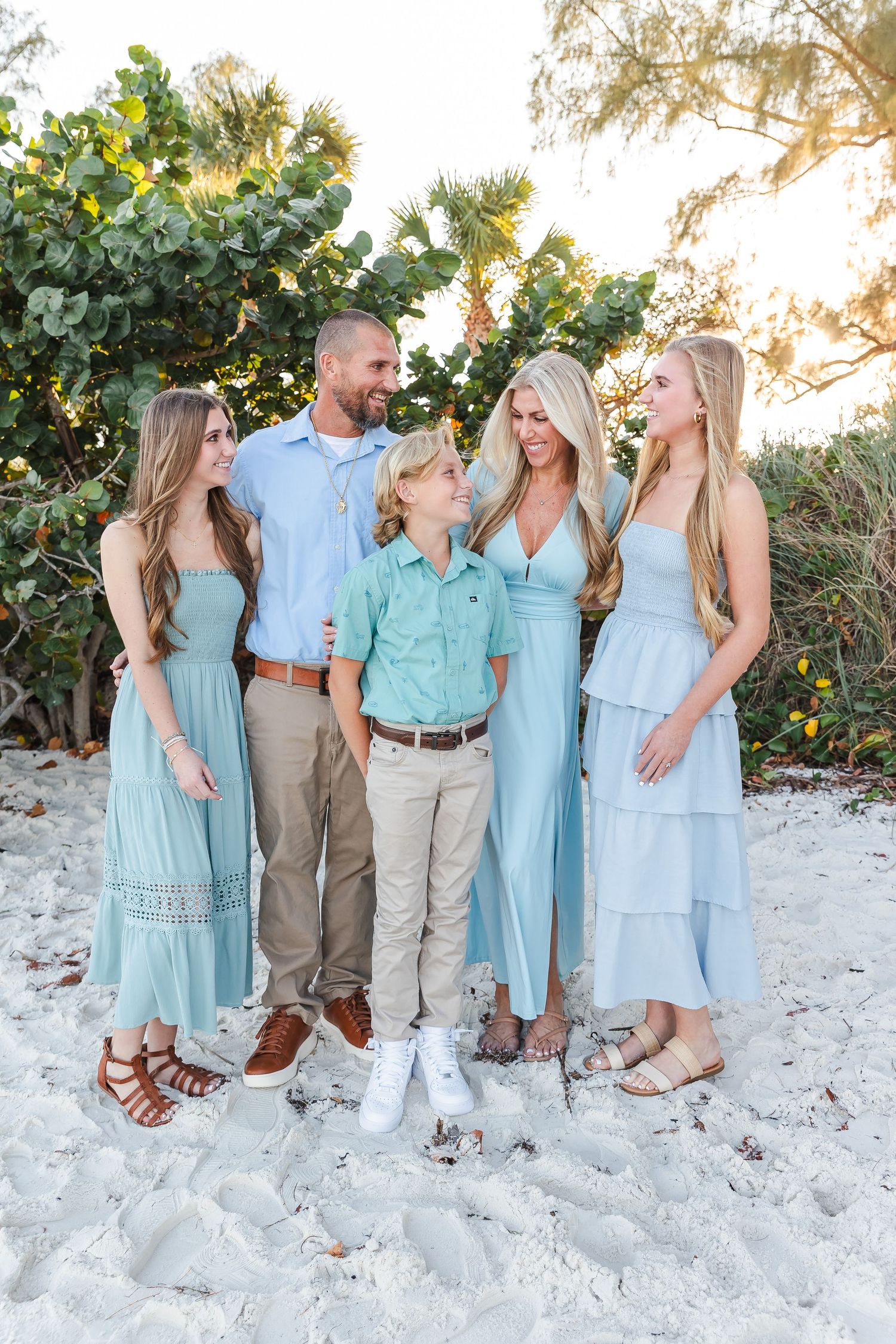 Family group wearing coordinated mint and blue outfits posing together on a white sandy beach.