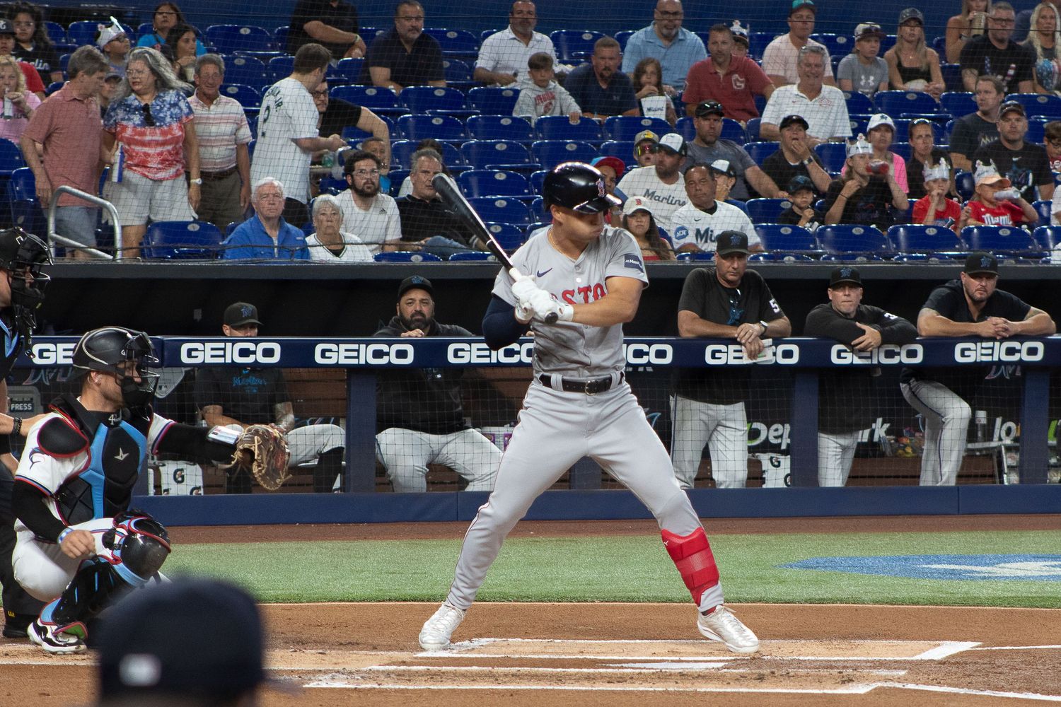 A baseball player at bat in a white uniform with red accents at a stadium.