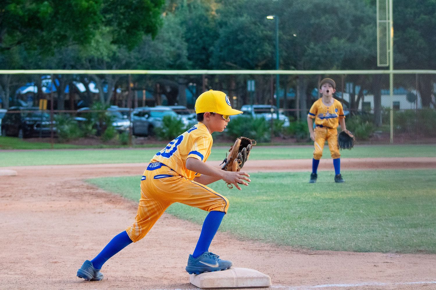 Young baseball player in yellow uniform taking a defensive stance at first base during a game.