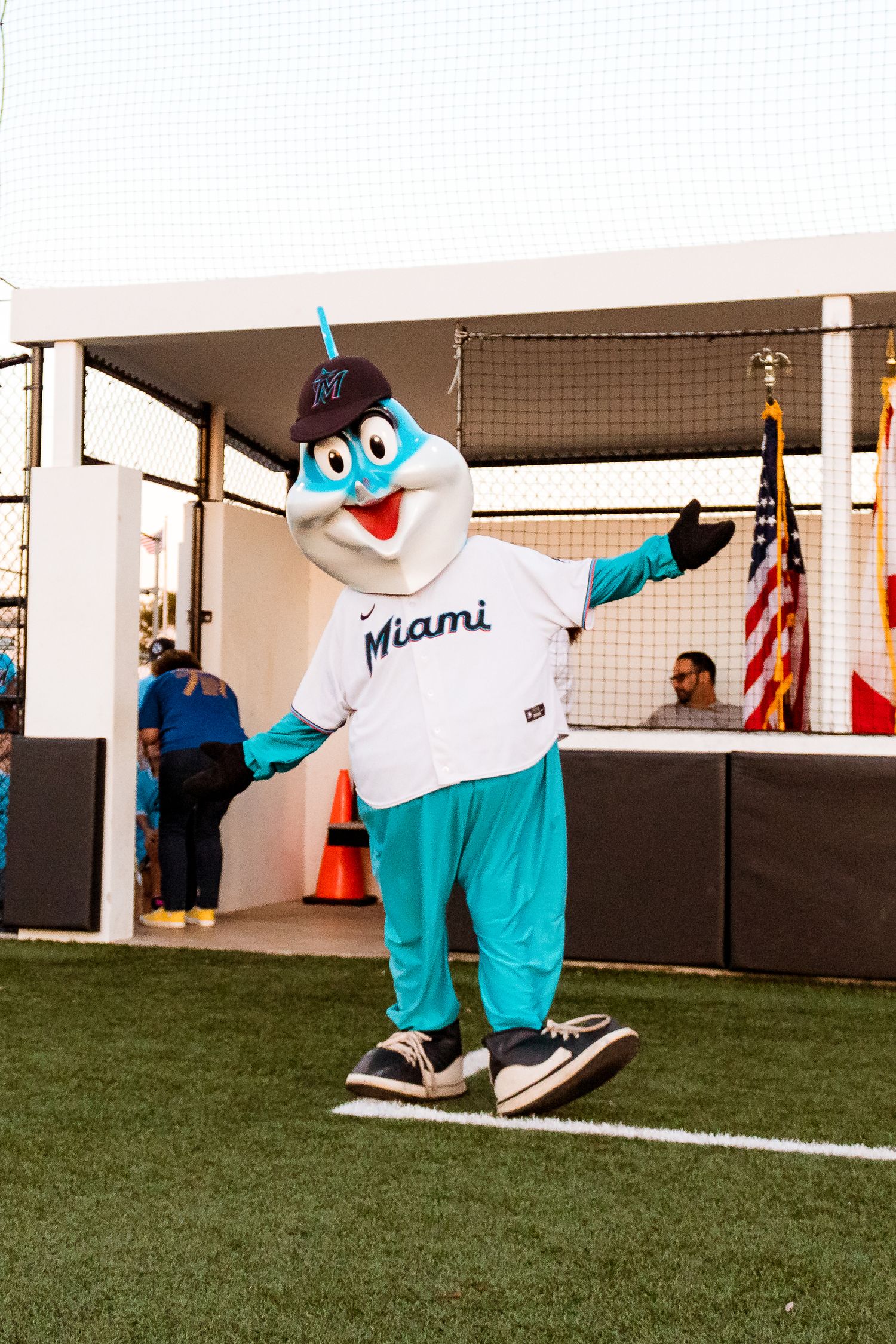 Miami sports mascot in teal and white uniform performing on a field near an American flag.