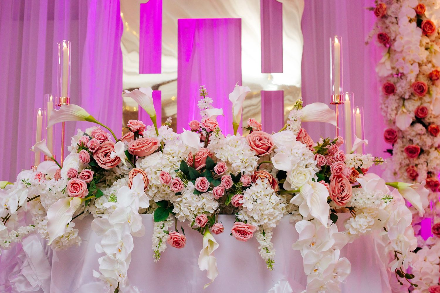 Luxurious floral arrangement with pink and white flowers adorned with candlesticks against a pink-lit backdrop.