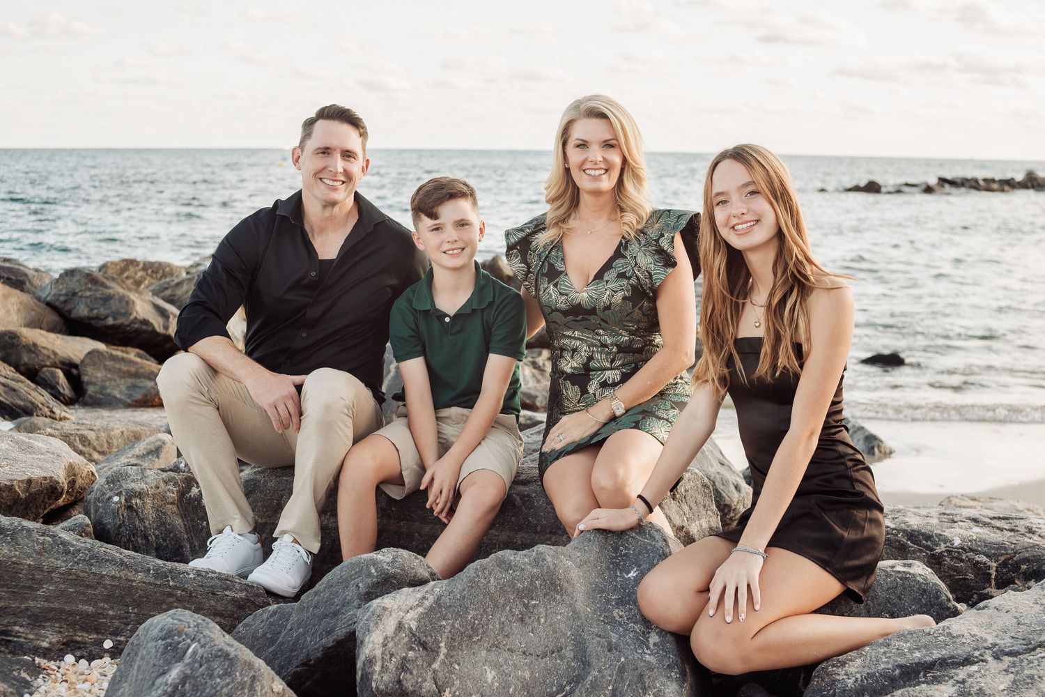 Family relaxes on rocky beach during golden hour with ocean waves in background.