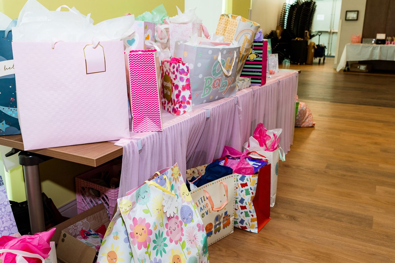 Pink and white gift bags displayed on wooden shelves with tulle decoration at a baby shower.