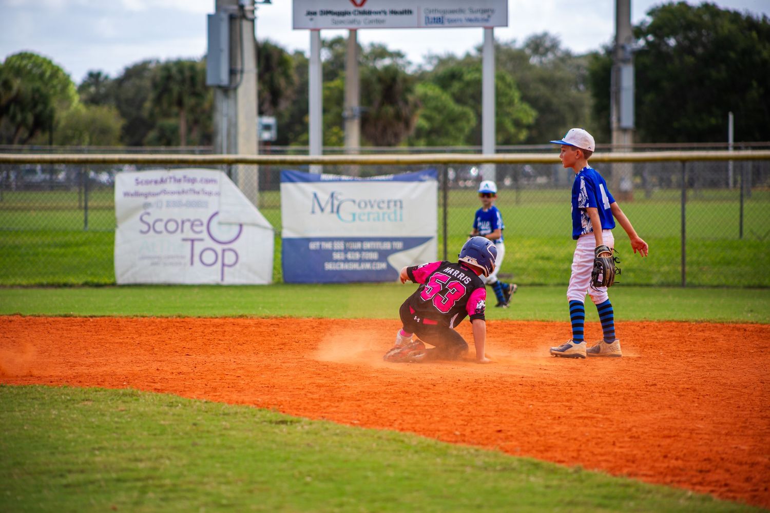 Youth baseball players compete in a series of action shots on a bright orange clay infield during a game.