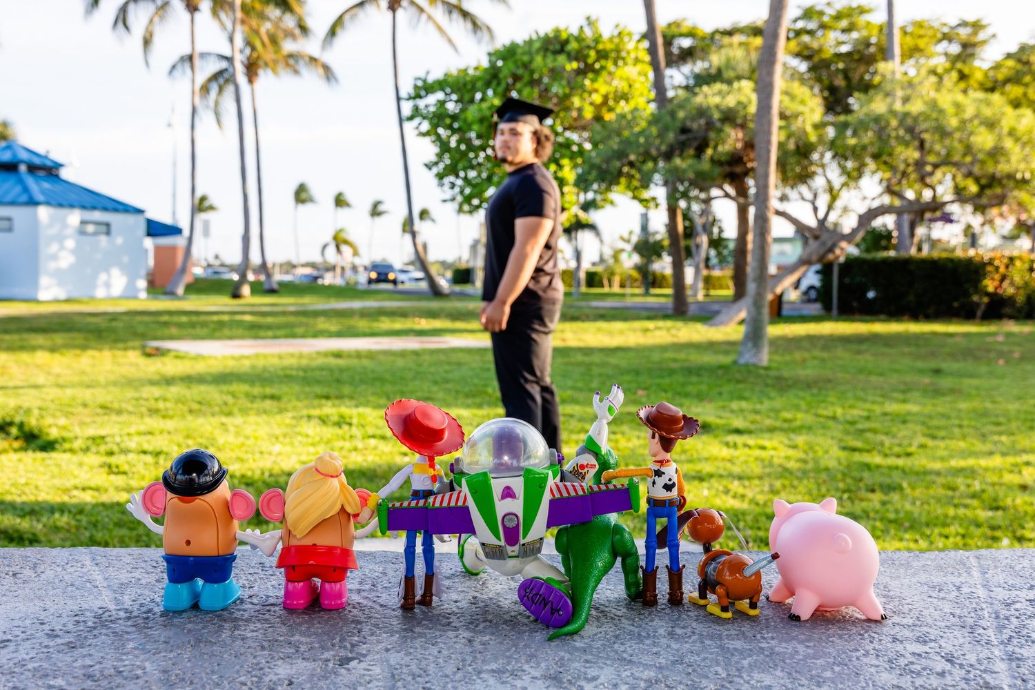Man standing outdoors on a path surrounded by colorful Toy Story character figurines including Buzz Lightyear and Woody.