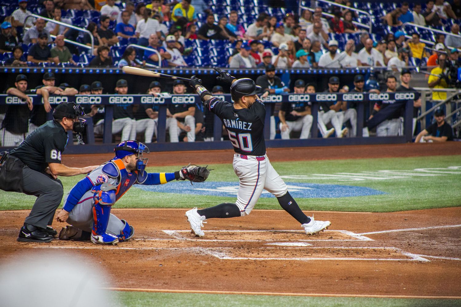 Baseball player in dark uniform takes powerful swing at home plate during night game.