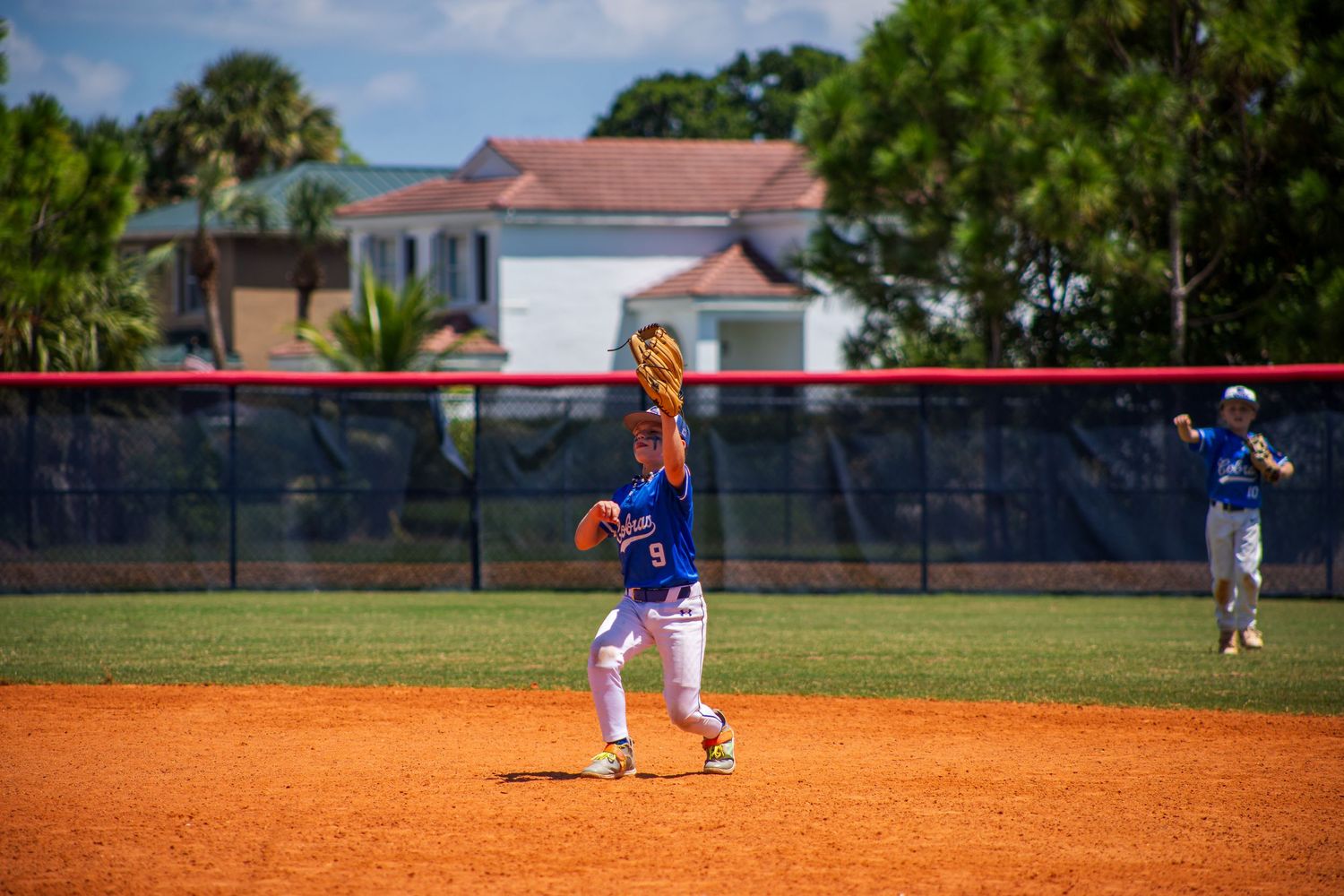 Players on a baseball field during a game with green grass and trees visible in the background.