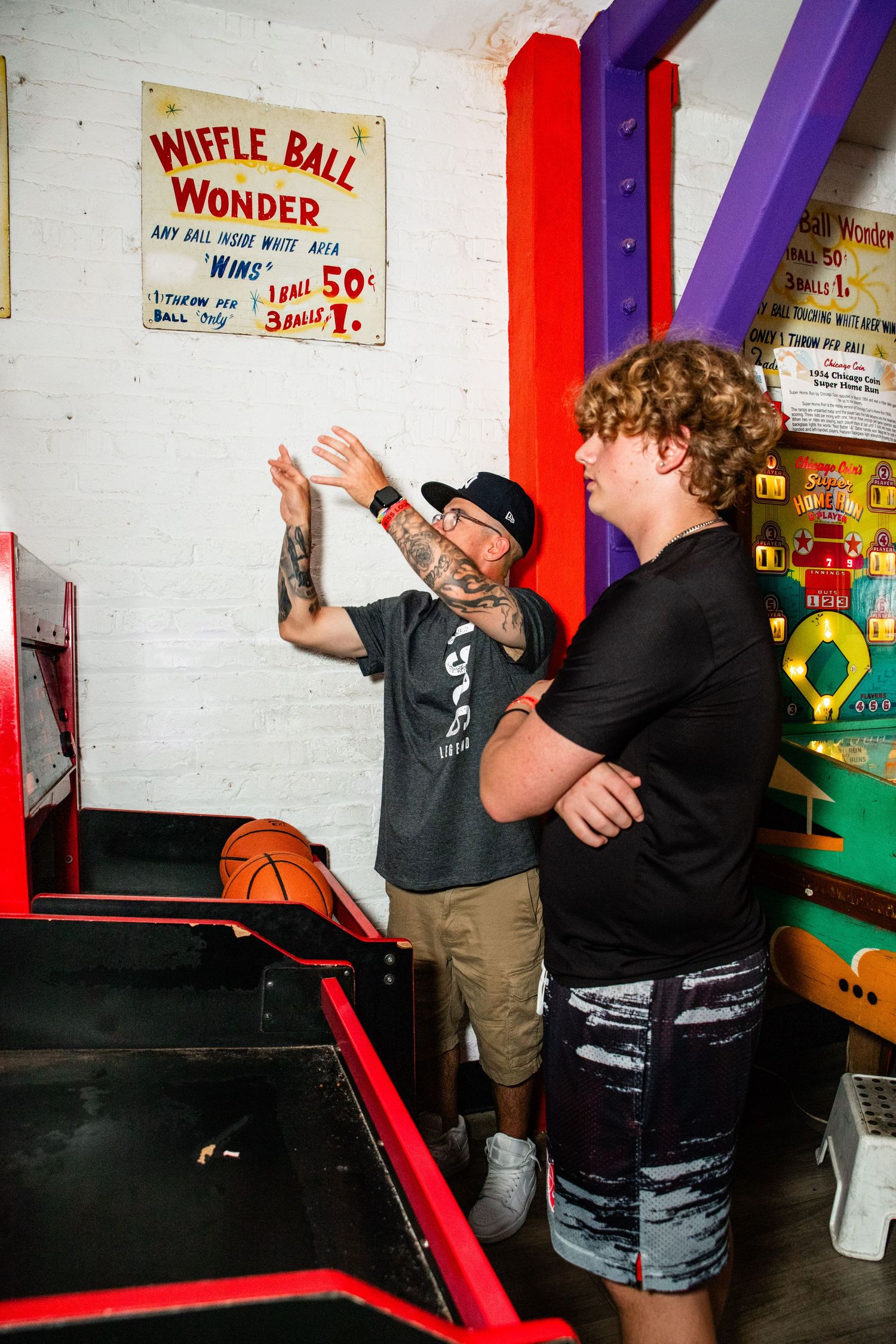 The image depicts two people playing a video game at an arcade-style machine in a colorful and lively indoor setting.