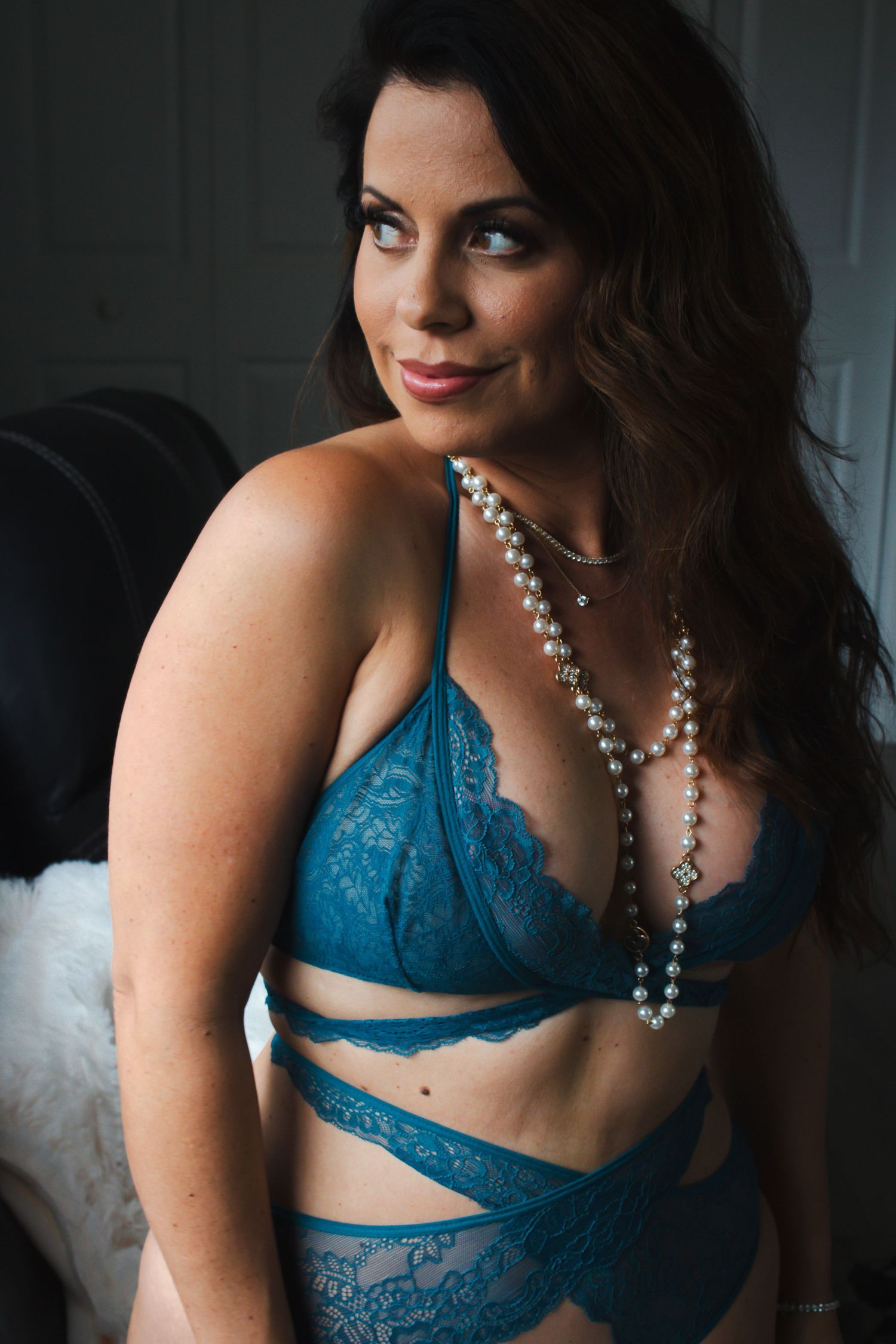 Intimate portrait featuring teal lace lingerie and delicate pearl jewelry against dark background.