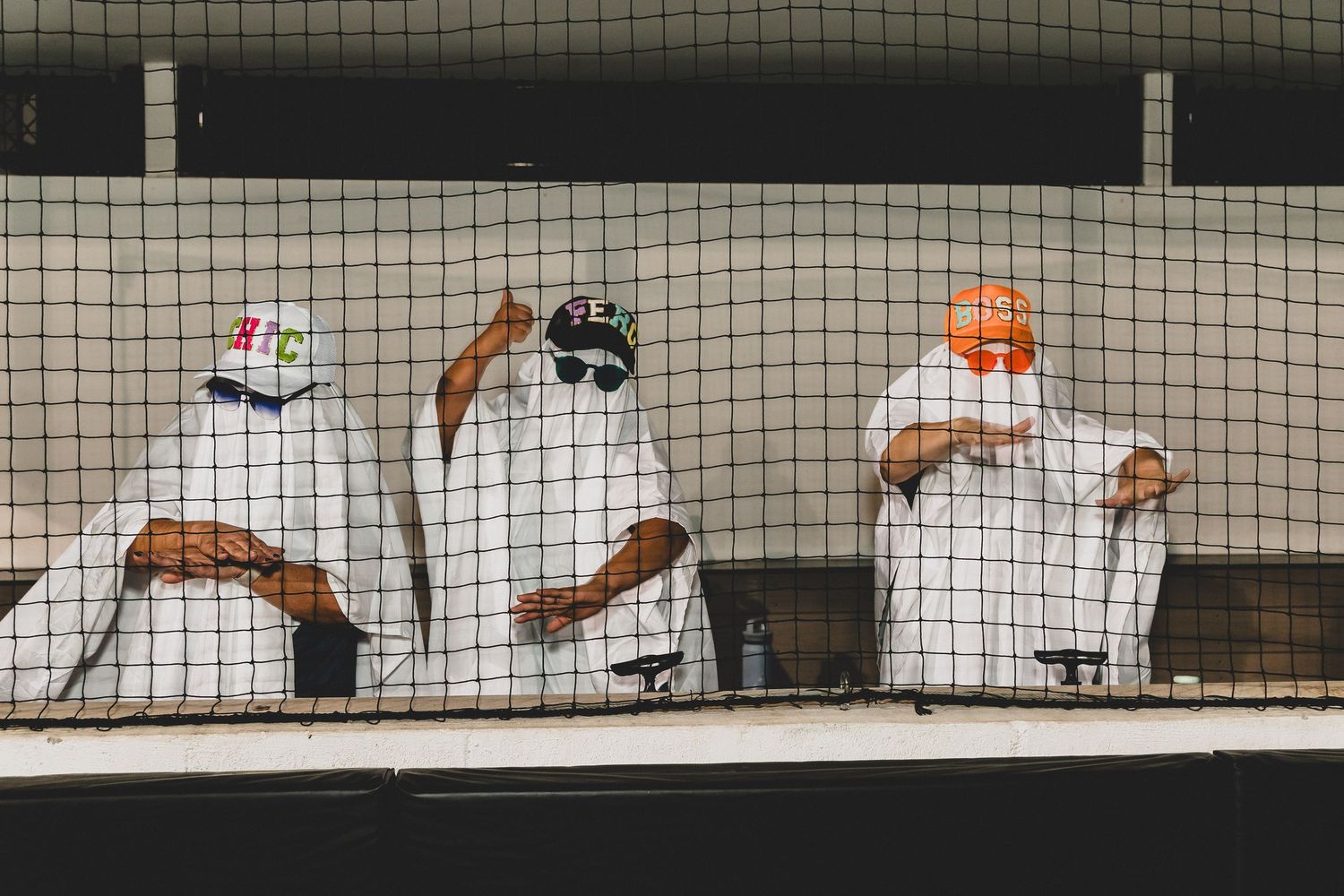Baseball players in white uniforms line up along a fence during a game or practice session.
