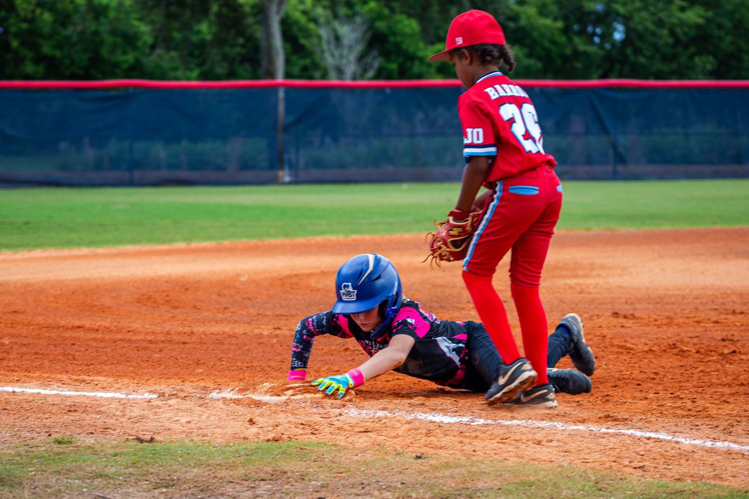 A close play at home plate during a softball game with players in red and blue uniforms.