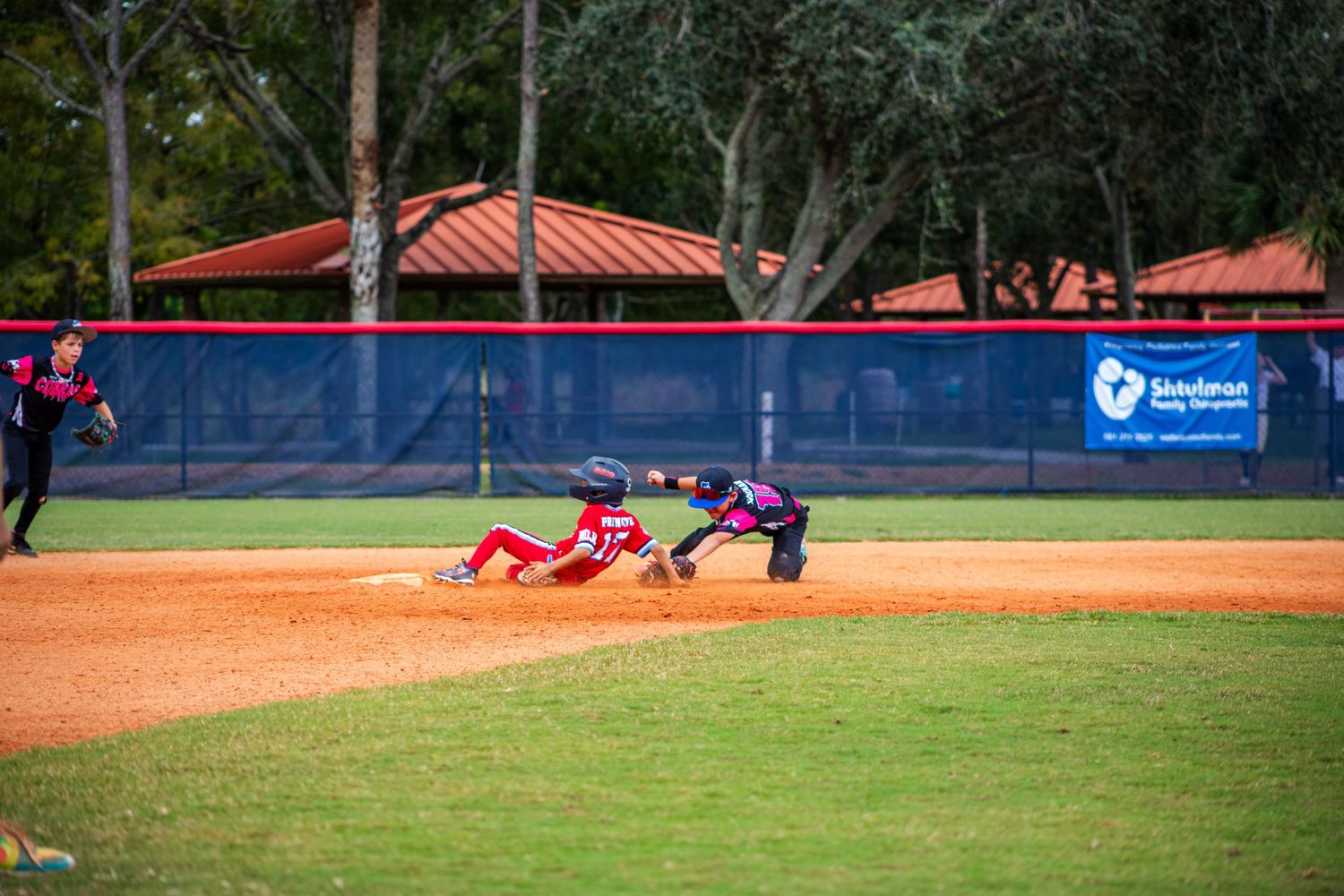 Baseball players competing on field with red dugout roof visible in background.