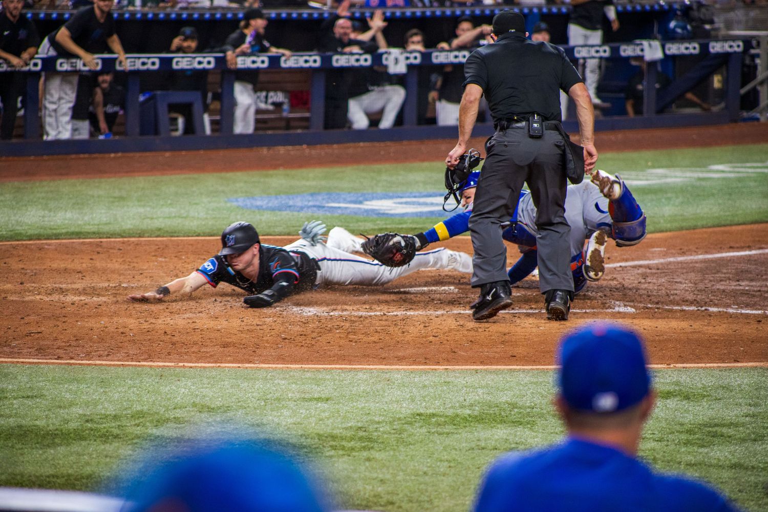 Baseball player slides into home plate as umpire watches for the call during intense play.