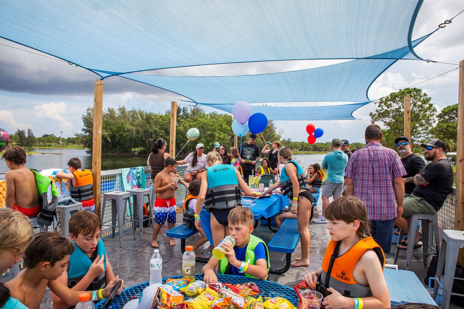 People enjoying drinks and socializing at an outdoor patio bar by the water on a sunny summer day.