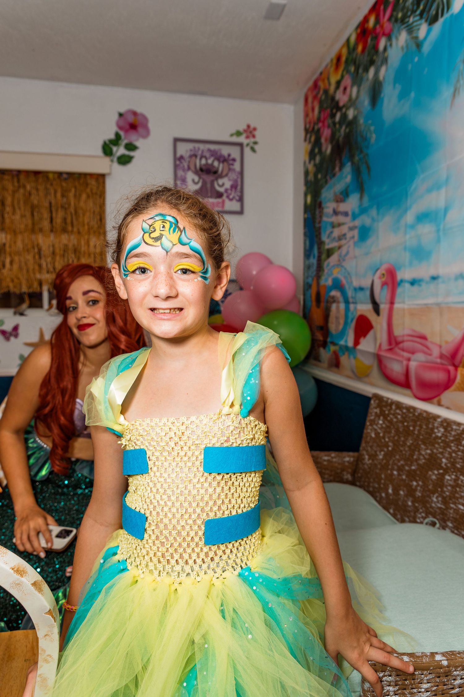 Happy child wearing a bright yellow and green party dress poses playfully during a celebration.