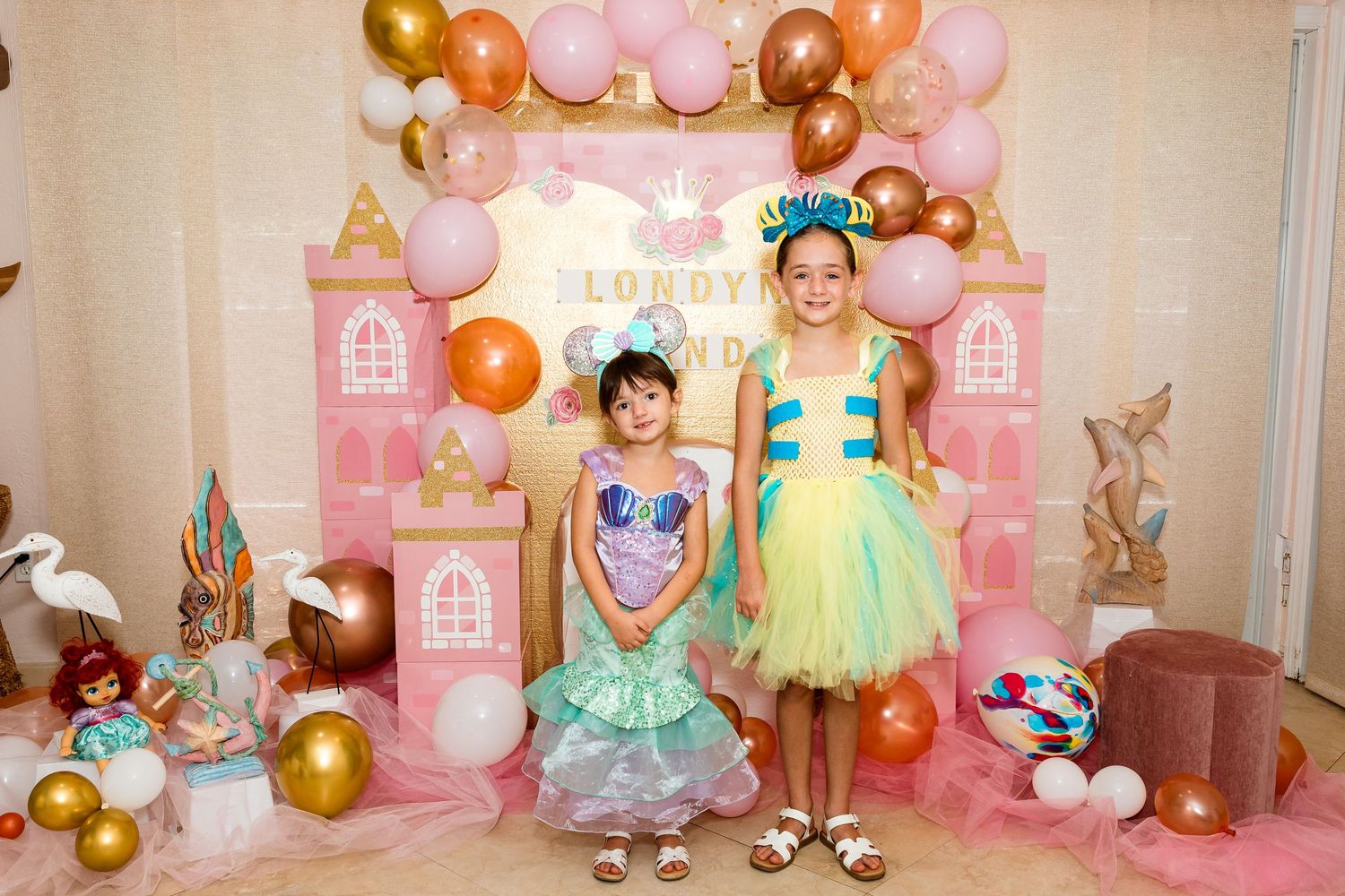 A princess-themed birthday party setup with a pink castle backdrop, balloon garland, and festive decorations.